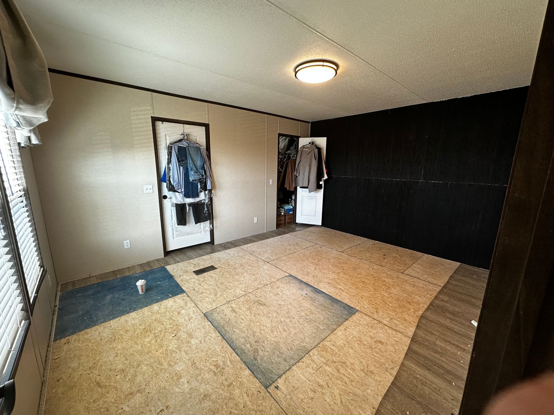 Empty room with beige walls, dark accent wall, wood floor, and a hanging coat by the door.