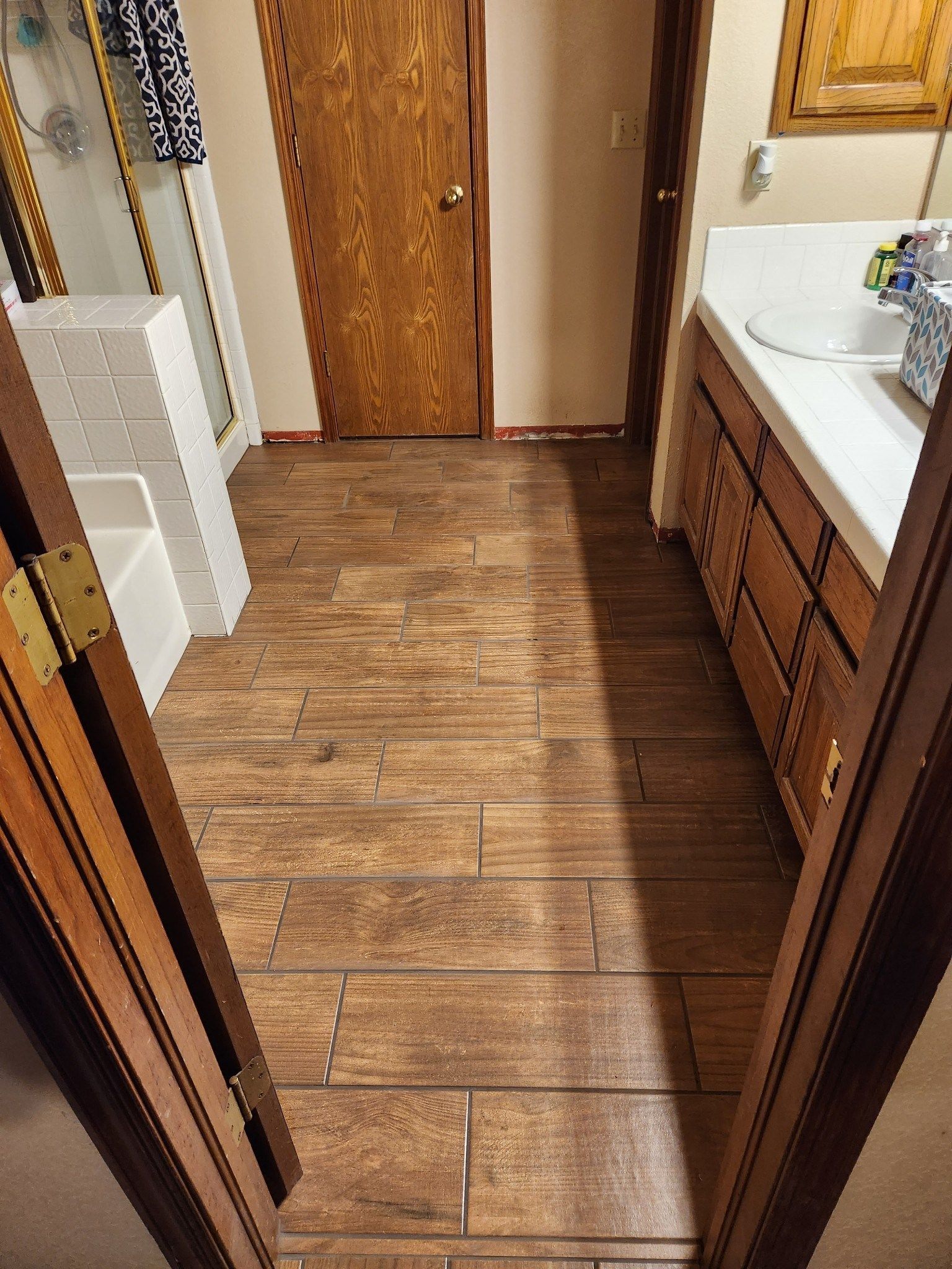 Narrow bathroom with wood-look floor, wooden door, white sink, and toilet visible on the left