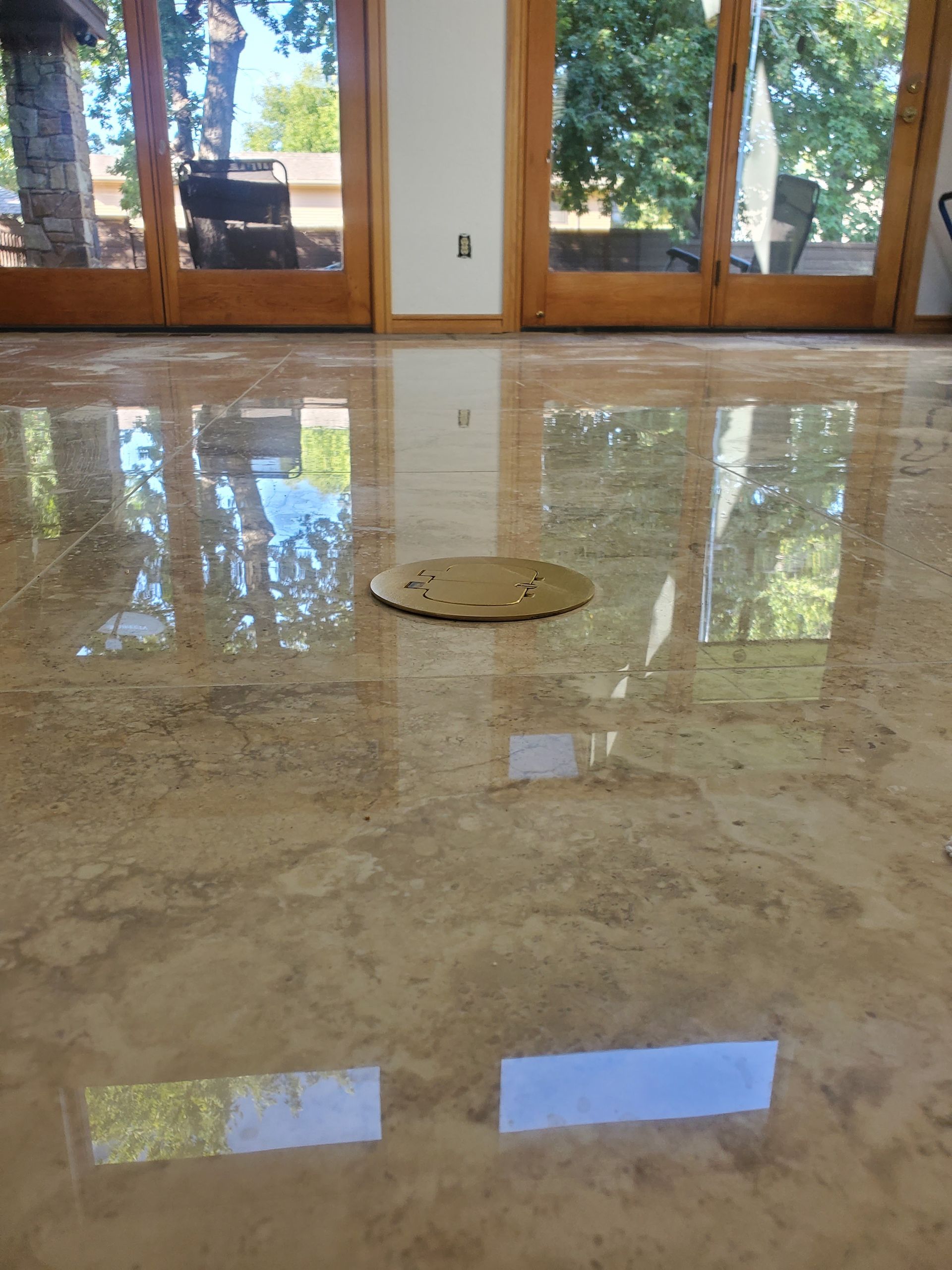 Glossy marble floor in a sunlit room with glass doors and a circular floor drain in the center.