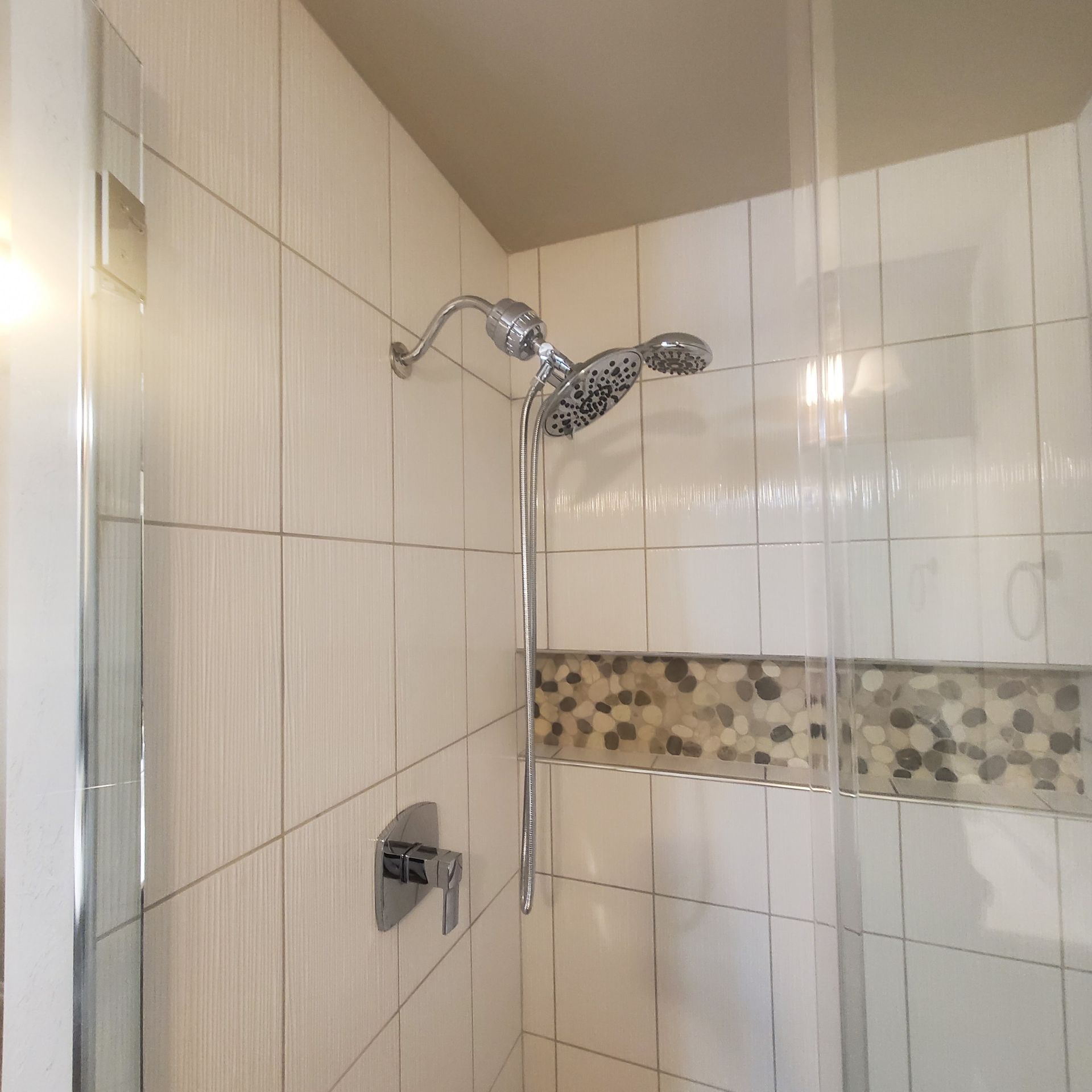 Shower stall with white tile walls, chrome showerhead, and decorative mosaic strip.