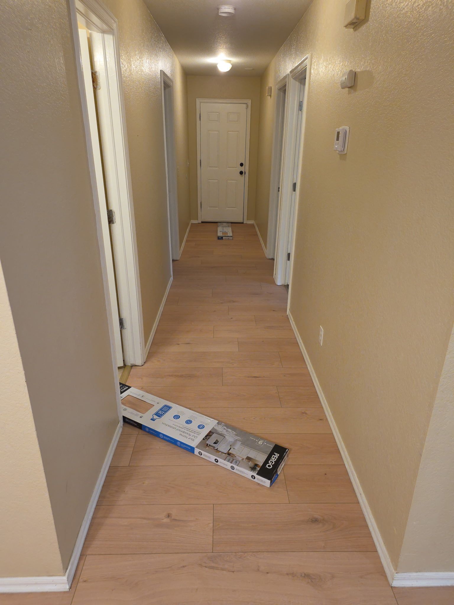 Hallway with tan walls and wood floor; a fallen package lies near the foreground.