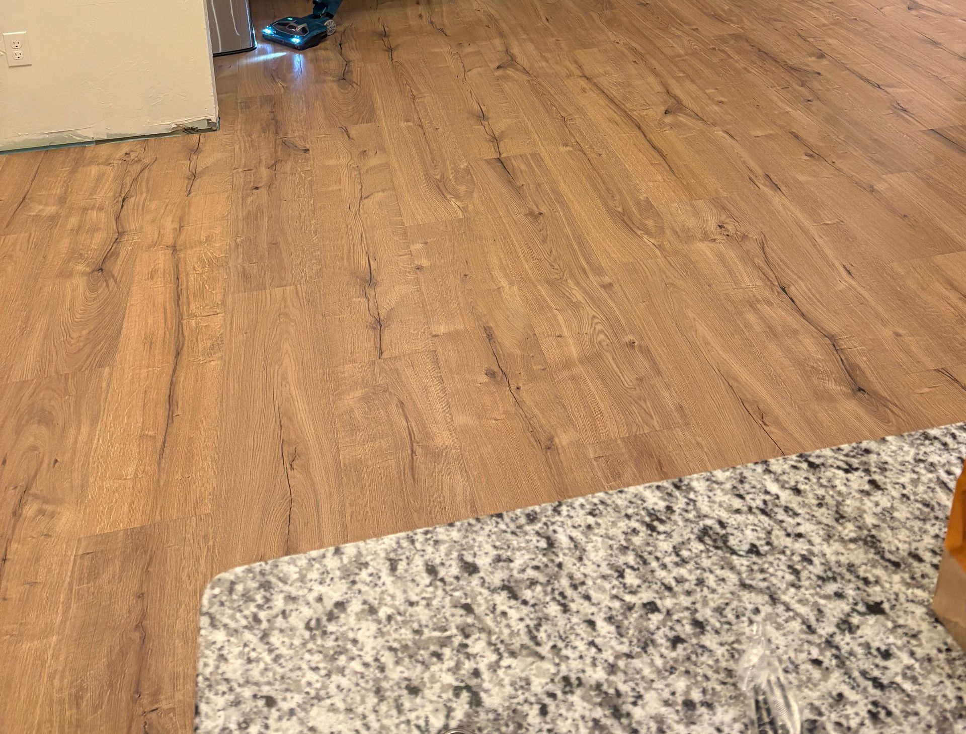 Wood flooring beside a speckled granite countertop, with a doorway in the background.