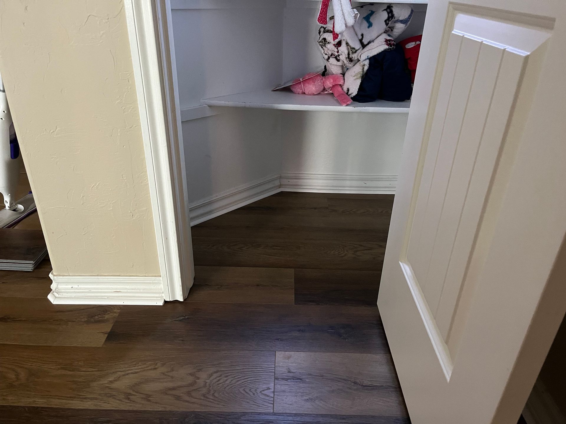 Open closet with white shelves and clothes, next to a dark wood floor and an open white door