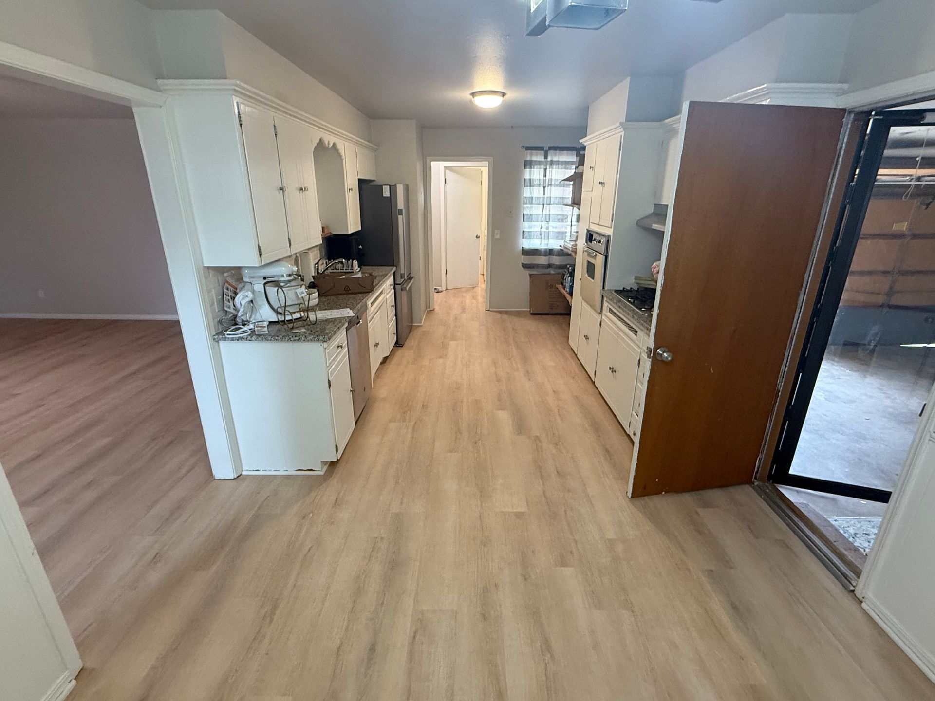 Open-plan kitchen and living area with light wood floors, white cabinets, and a sliding glass door.