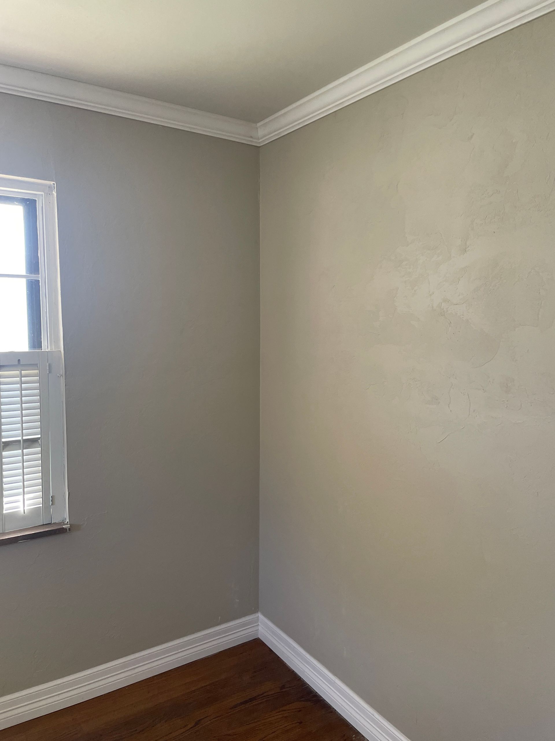 Empty gray room corner with white trim, a window, and hardwood floor.
