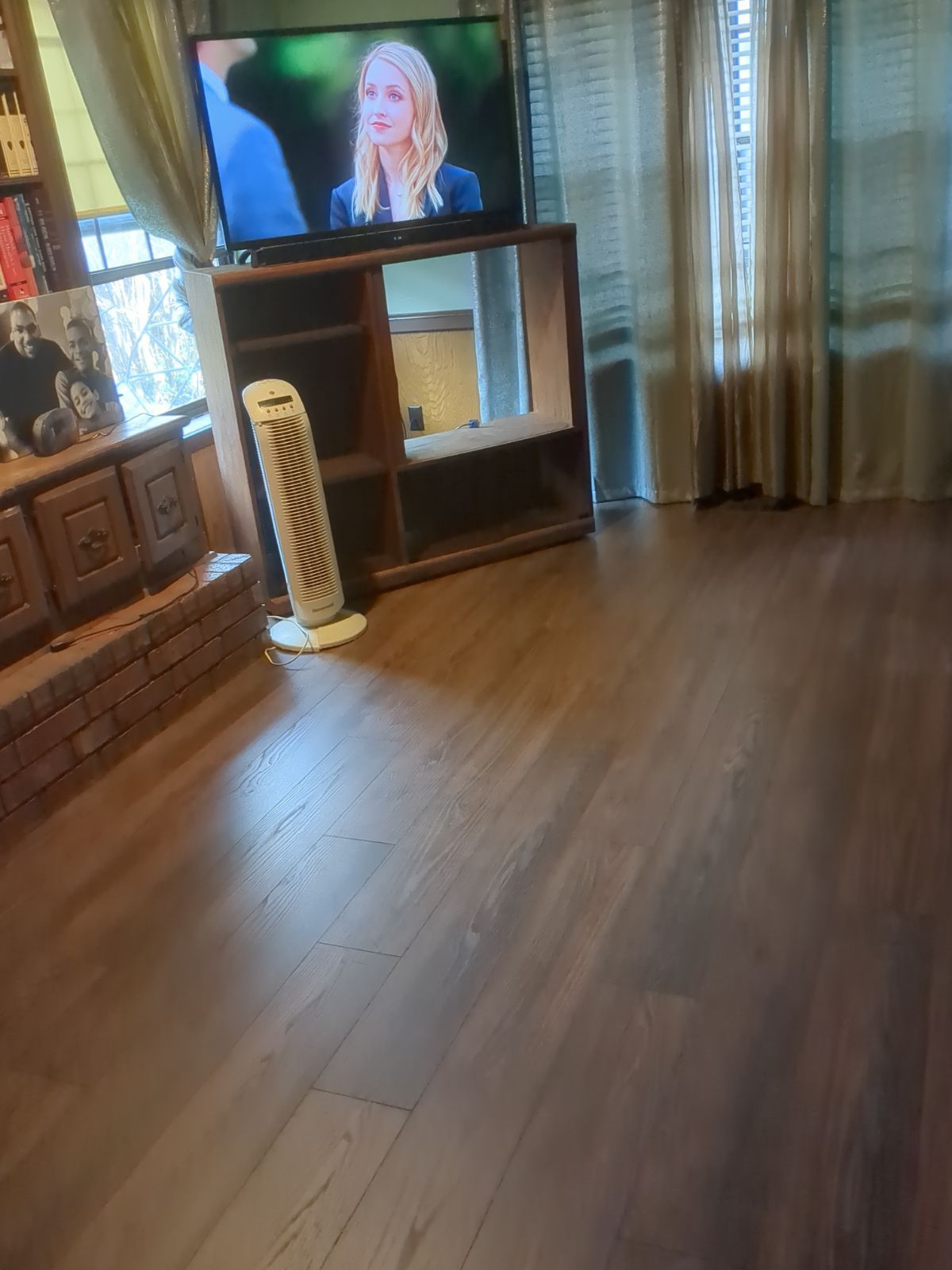 Living room with hardwood floor, TV on cabinet, and sheer curtains by a window.