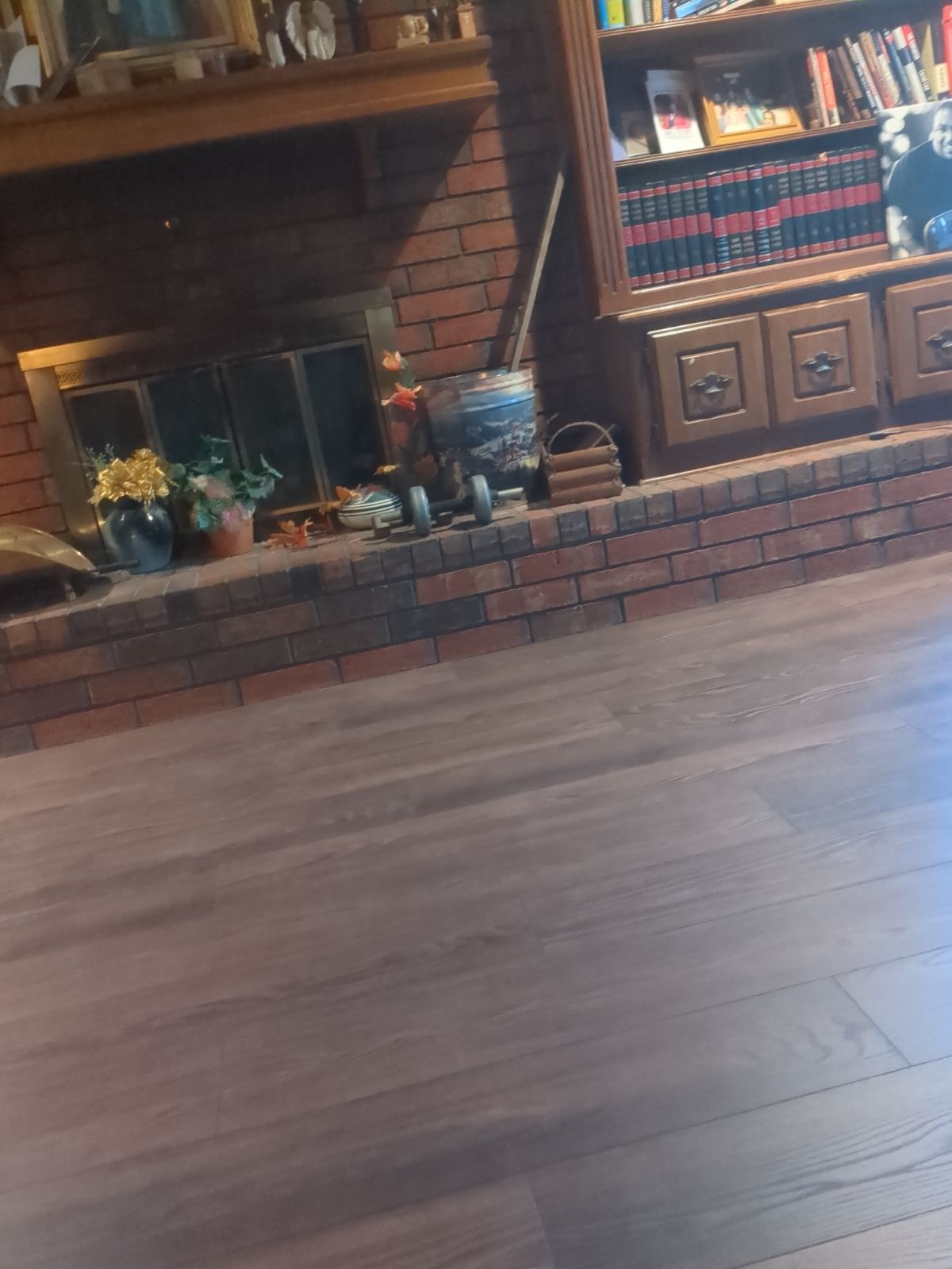 Living room with brick fireplace, wooden mantel, cabinet, and hardwood floor
