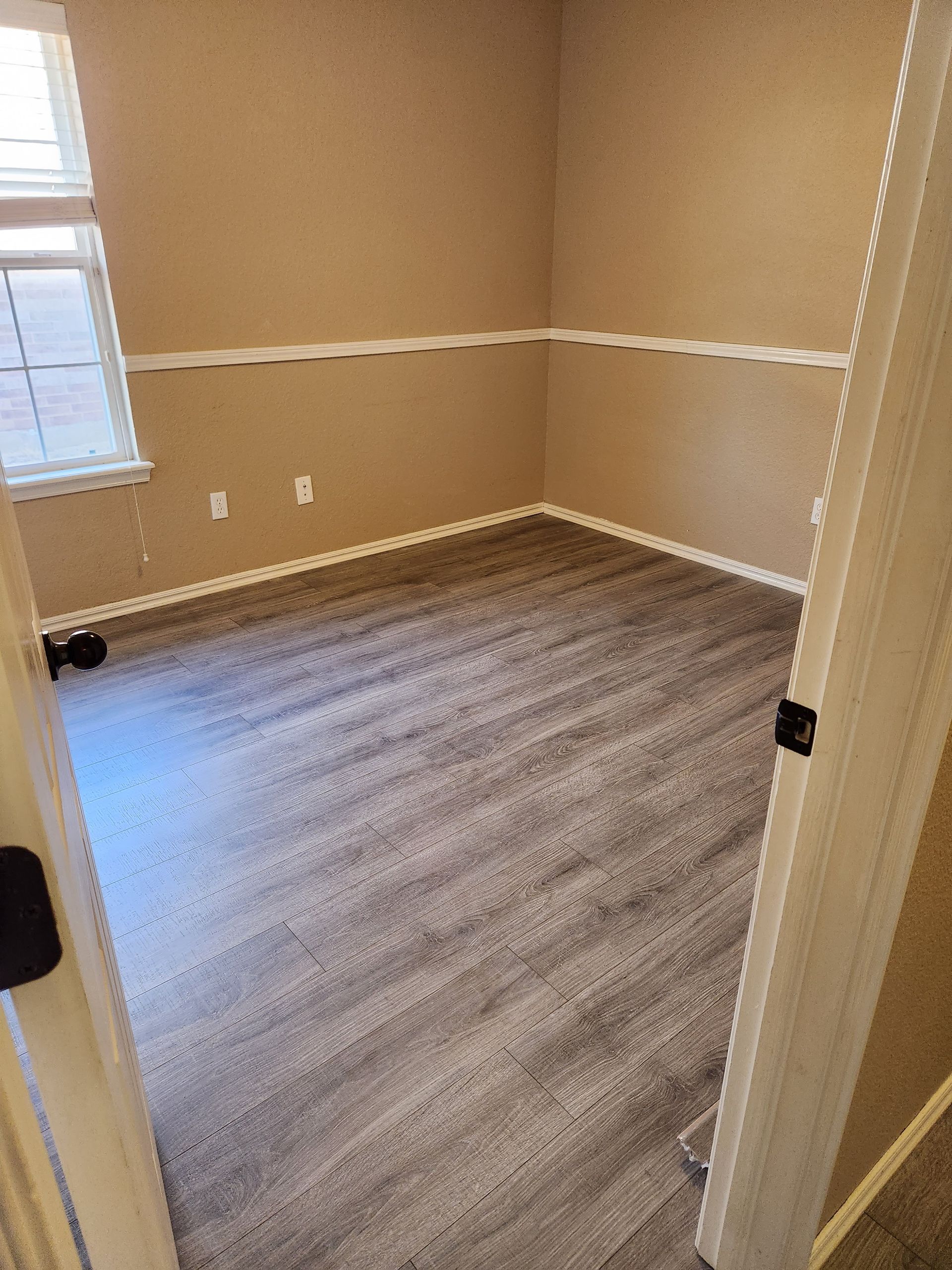 Empty beige room with gray carpet, white trim, and a window on the left side.