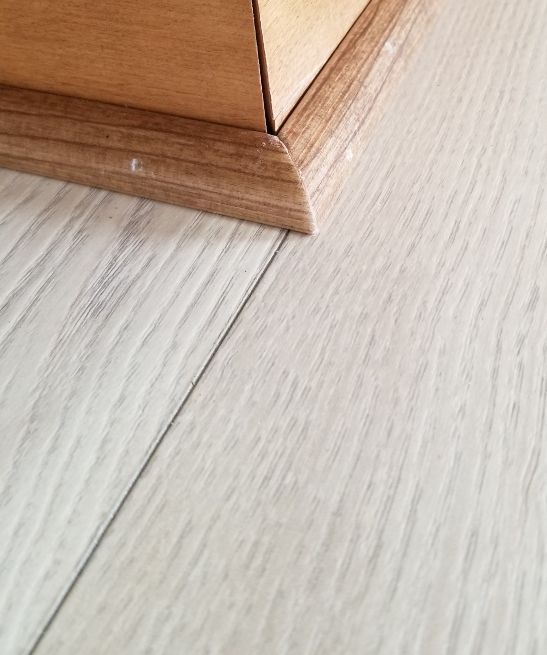 Wooden furniture base on light wood floor with a visible seam line