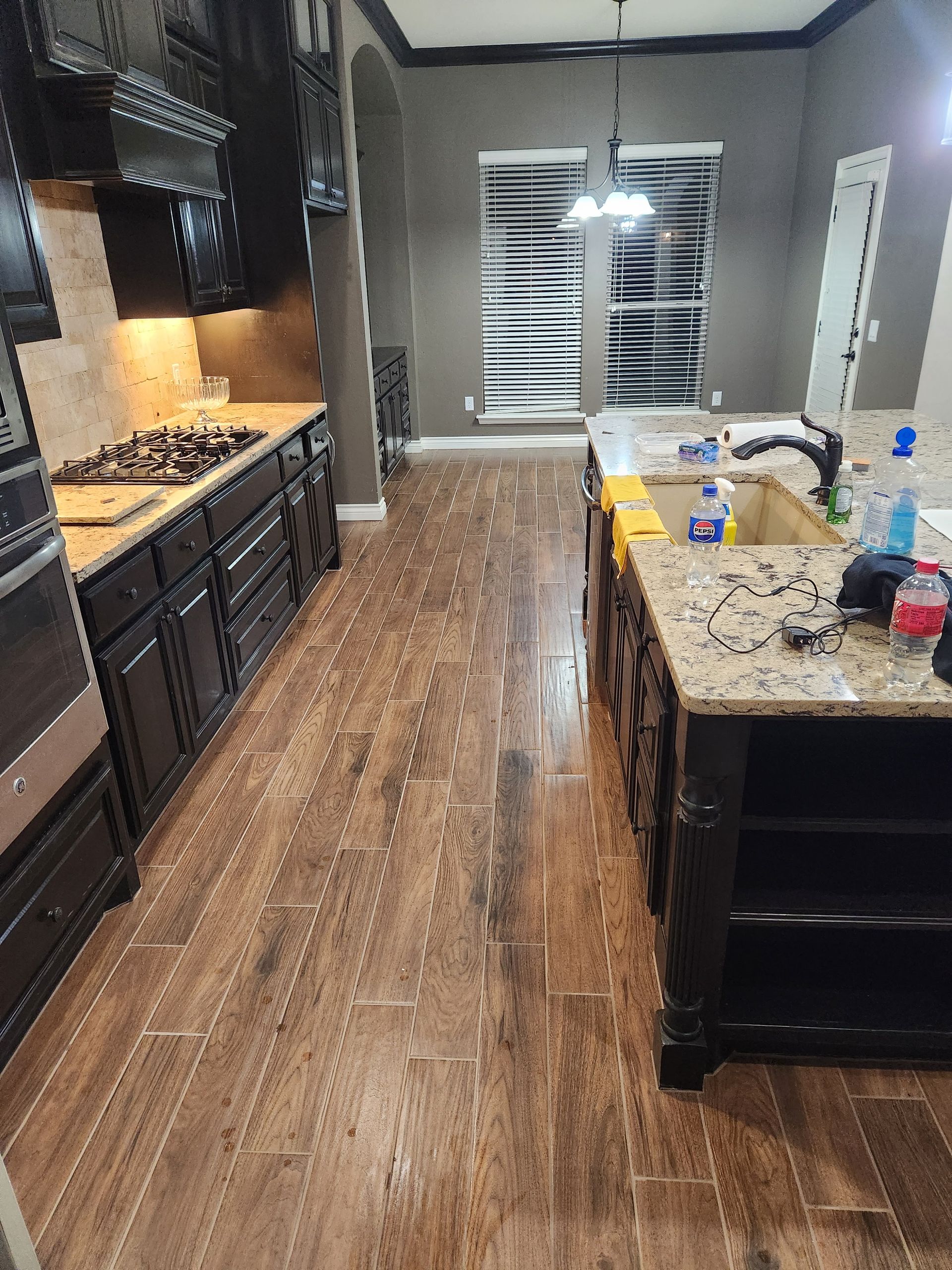Modern kitchen with dark cabinets, granite island, wood floor, and pendant light near a window.