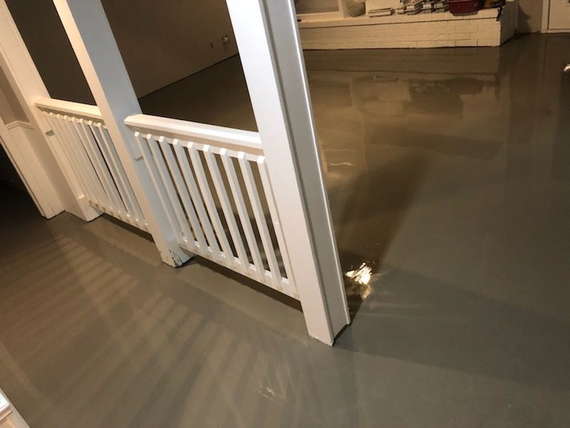 White baby gate blocking a doorway with gray flooring and a reflective glass door nearby