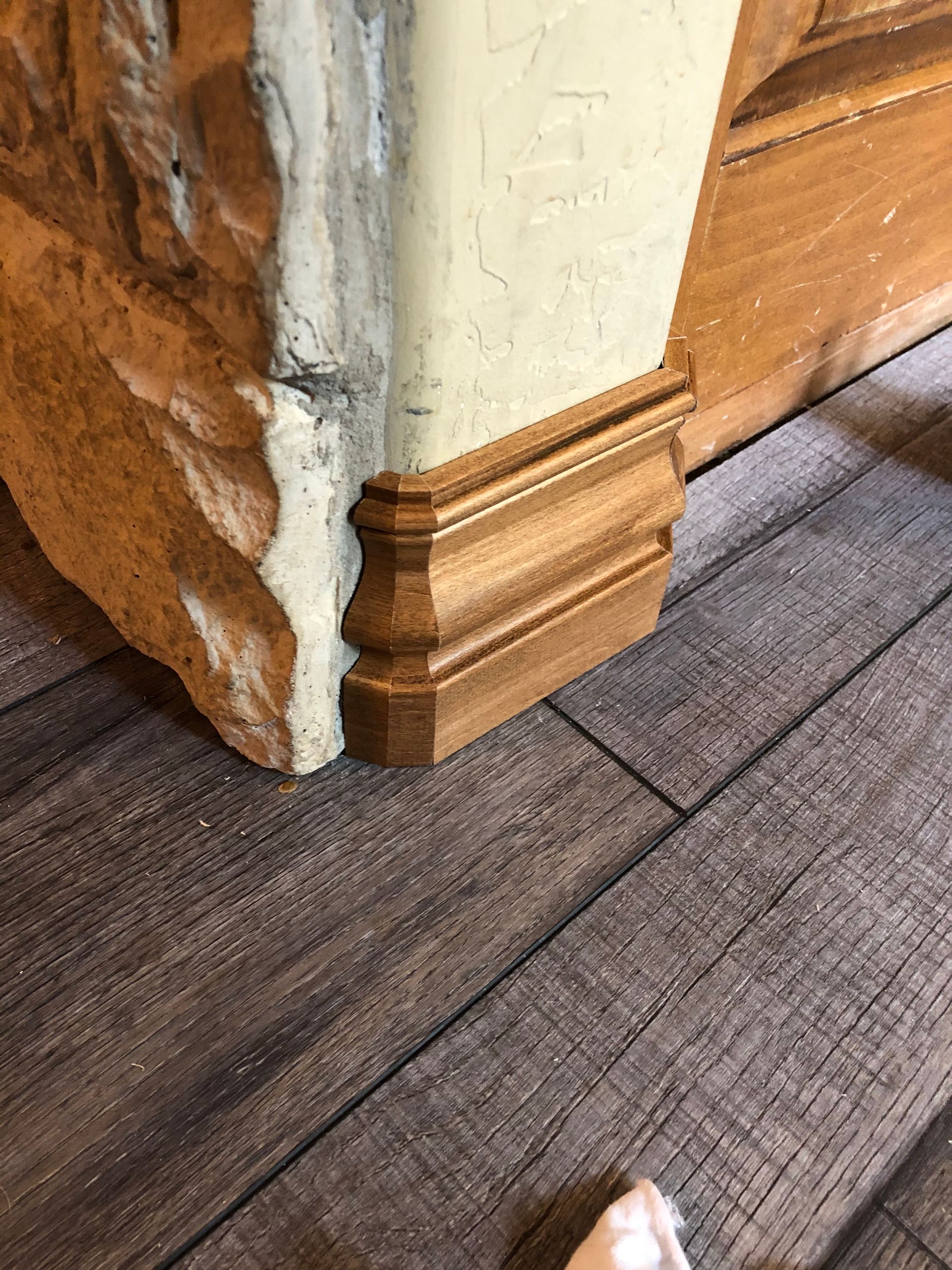 Corner of a stone wall with tan base molding beside a gray wood floor