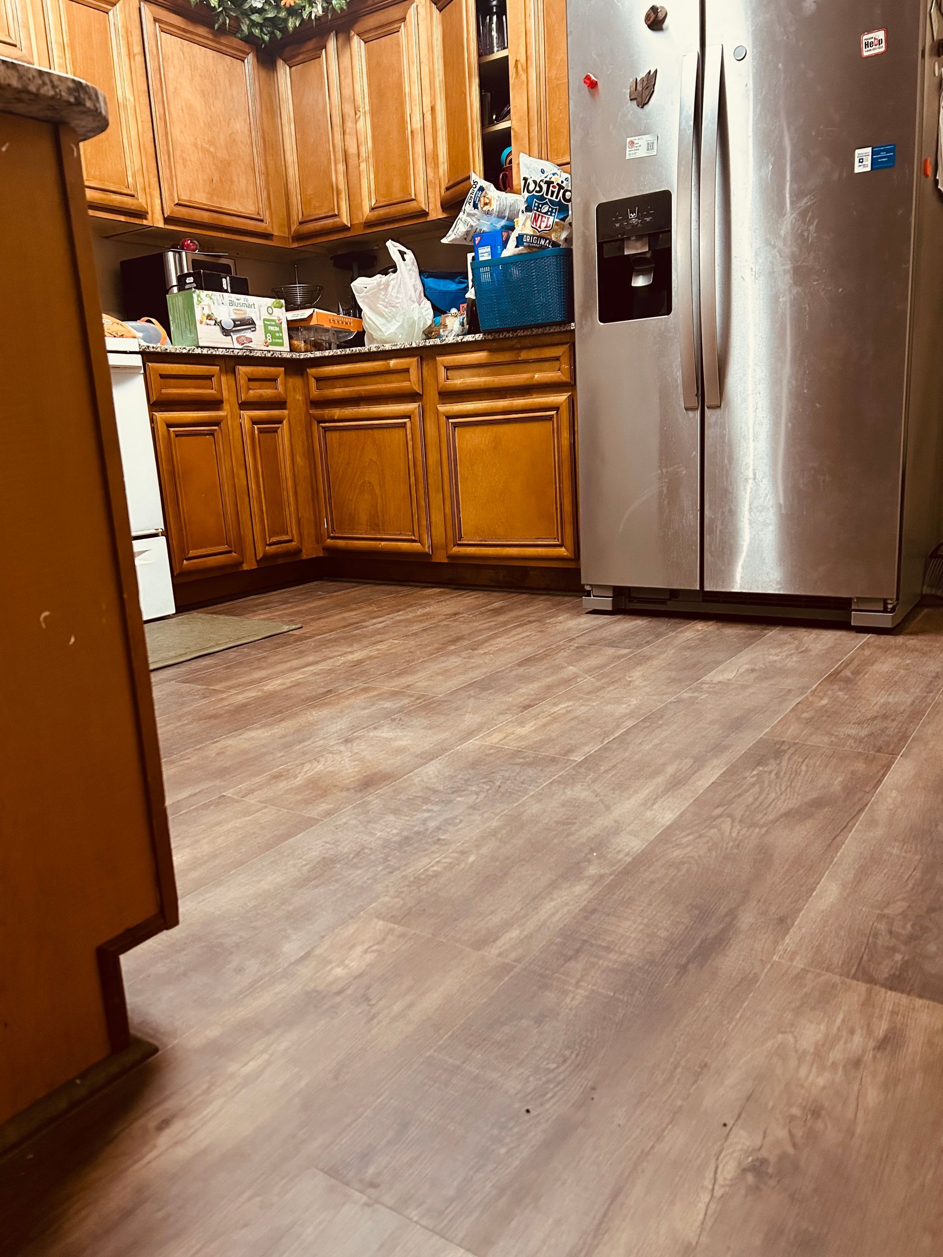 Wooden kitchen with stainless steel refrigerator and wood-look floor, viewed from the doorway