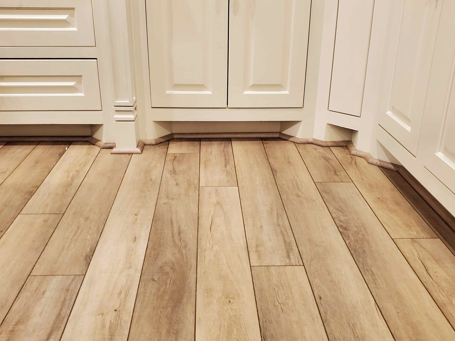 Light wood kitchen floor with white cabinets along the walls