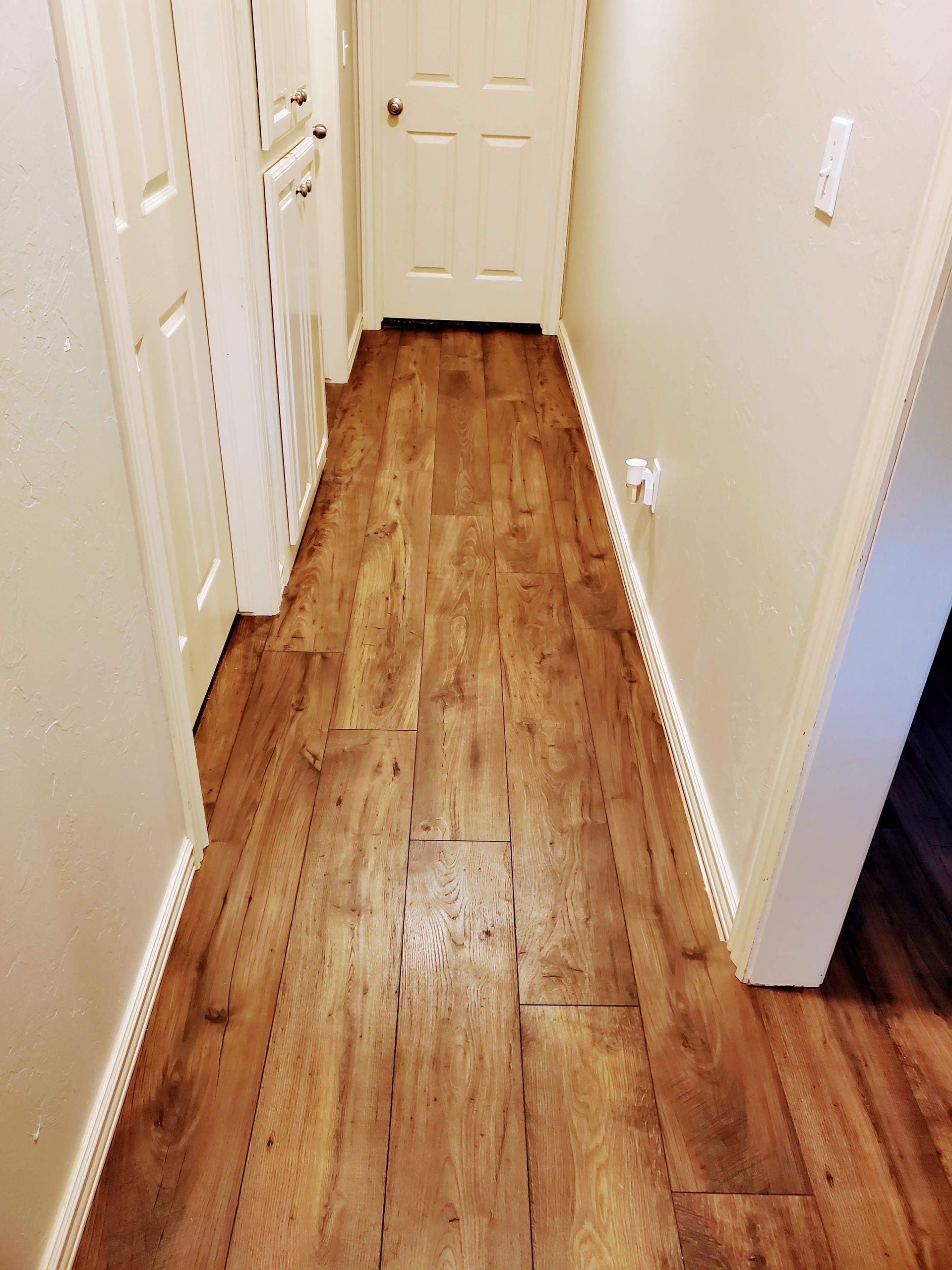 Narrow hallway with wood flooring, white walls, and doors at the end.