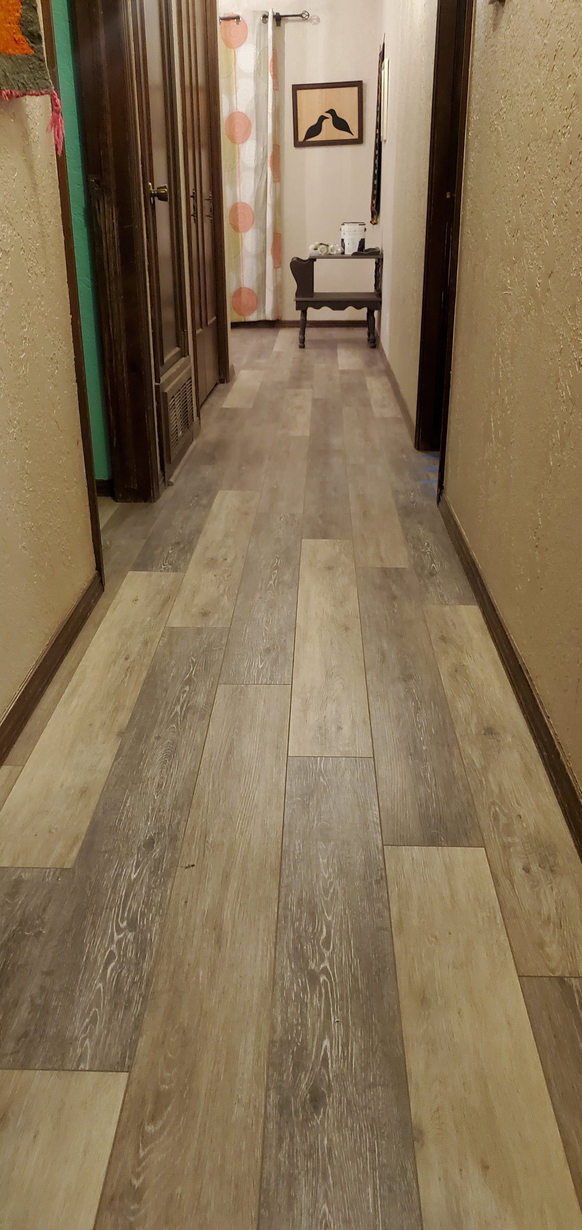 Narrow hallway with wood-look flooring, curtains, and a small chair at the far end