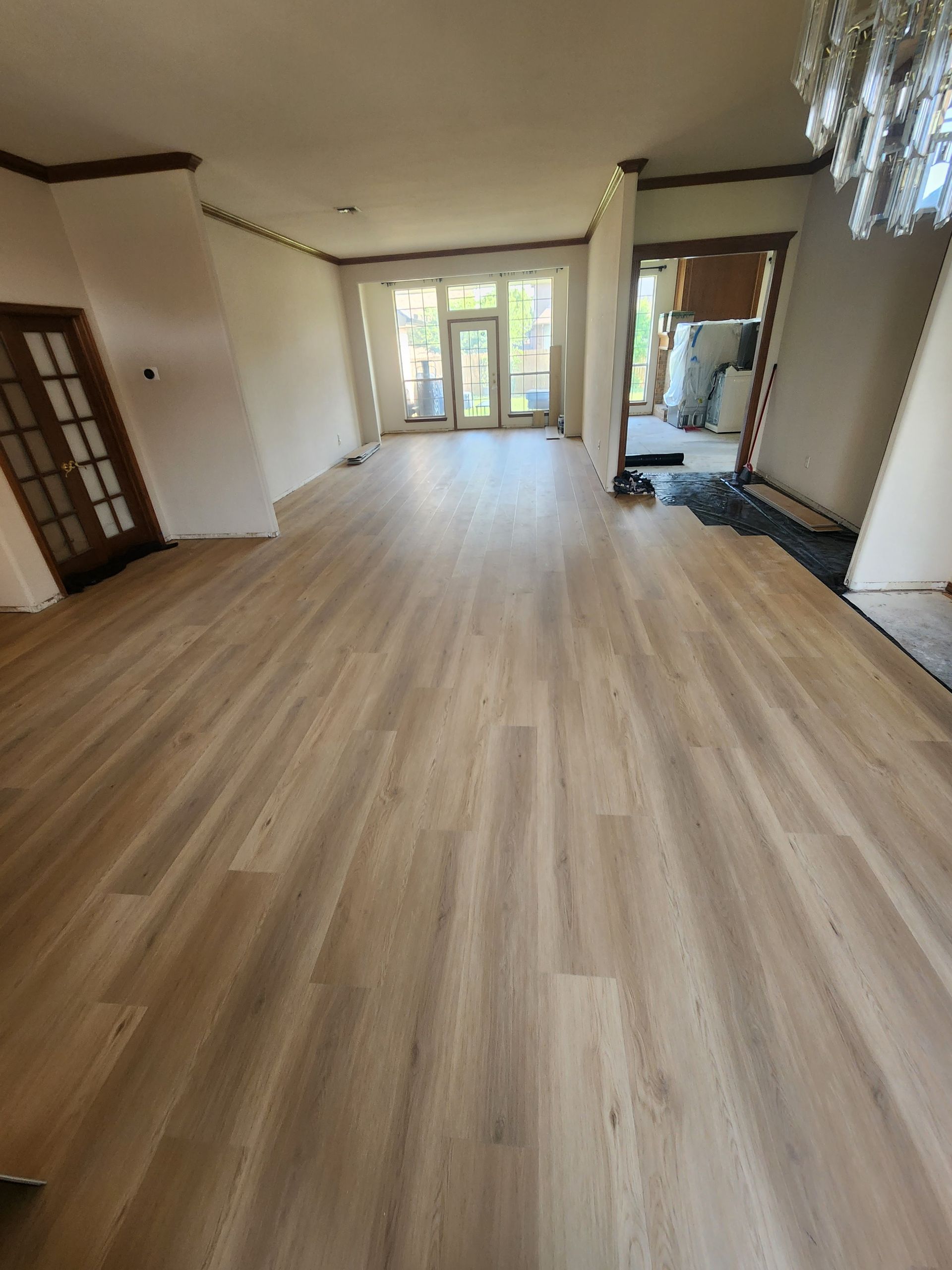 Spacious empty room with light wood flooring, white walls, a wall mirror, and glass doors at the far end.