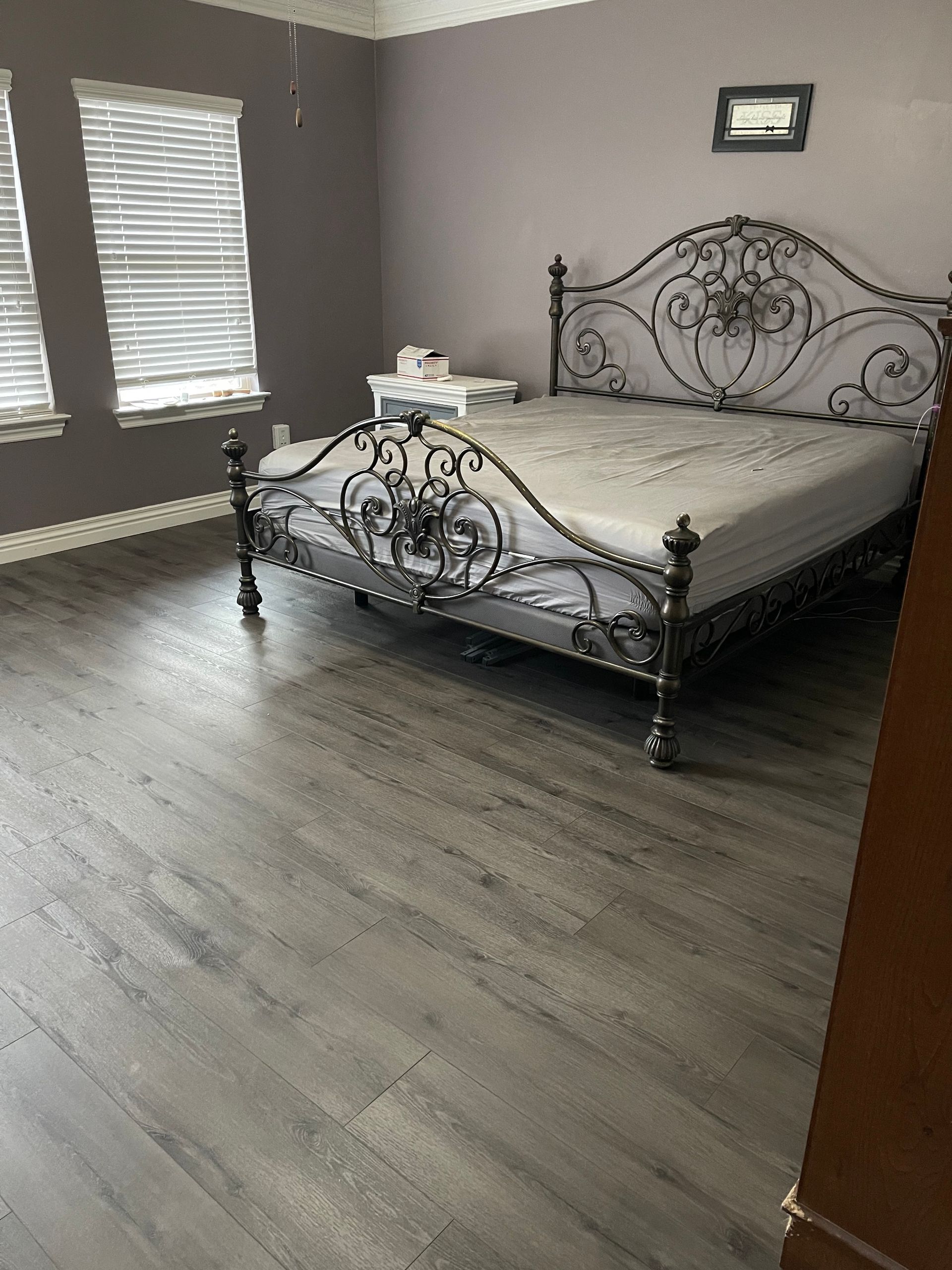 Empty bedroom with a wrought-iron bed, gray walls, and wood-look flooring
