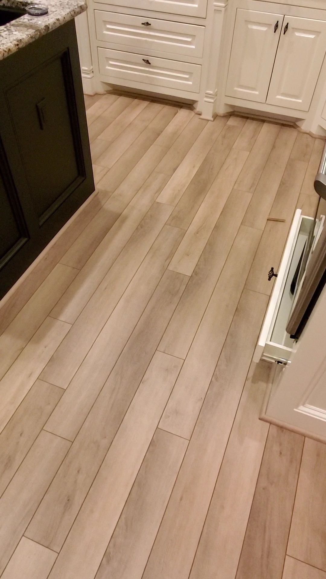 Narrow kitchen walkway with light wood floors and white cabinets on both sides