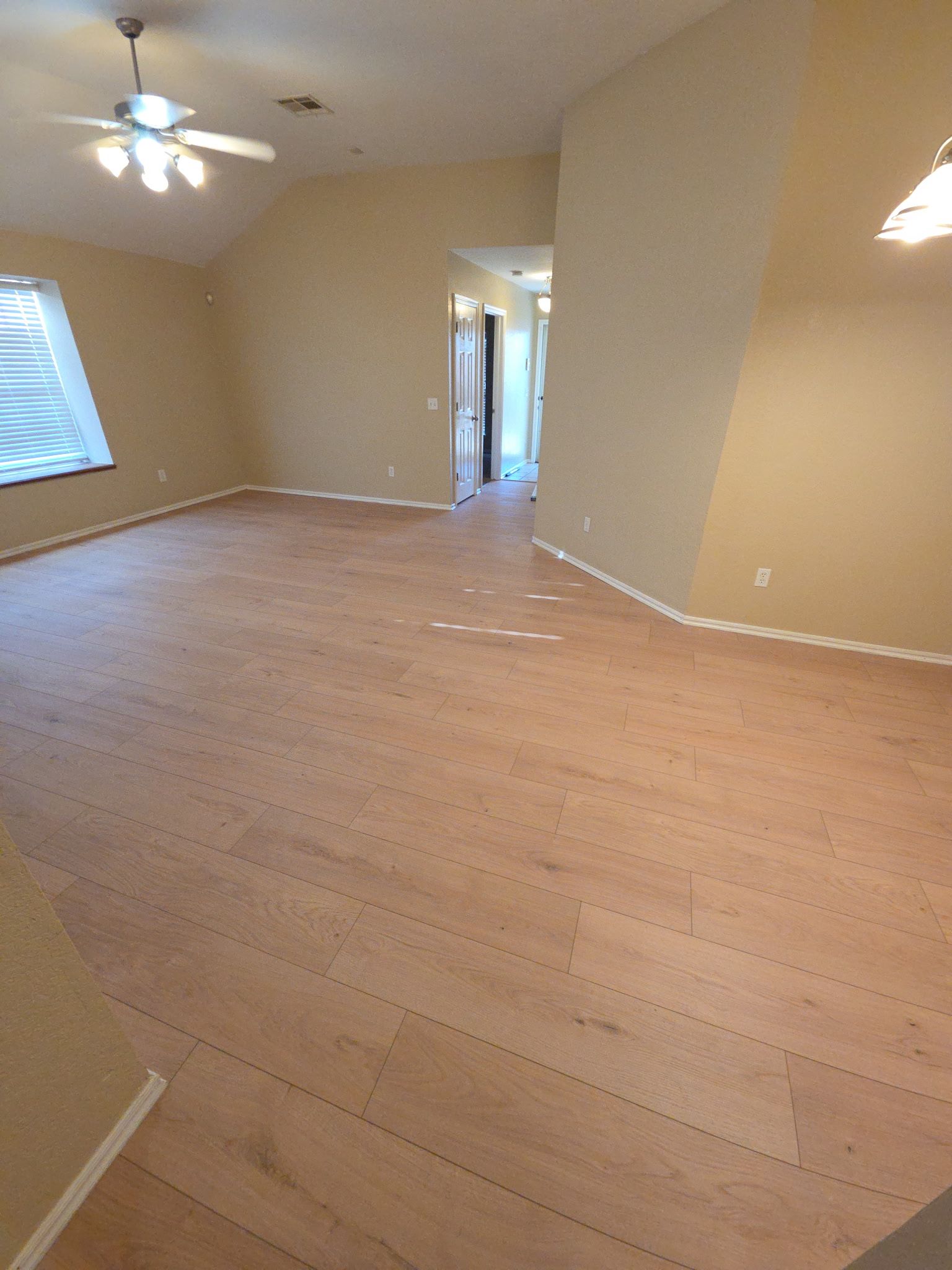 Empty beige living room with wood floors, ceiling fan, and a window letting in daylight