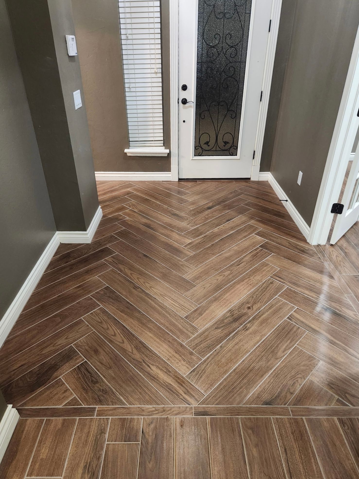 Wooden herringbone floor leading to a white front door in a hallway