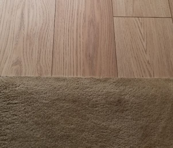 Wooden floor meeting a beige carpet edge, showing the transition between rooms.