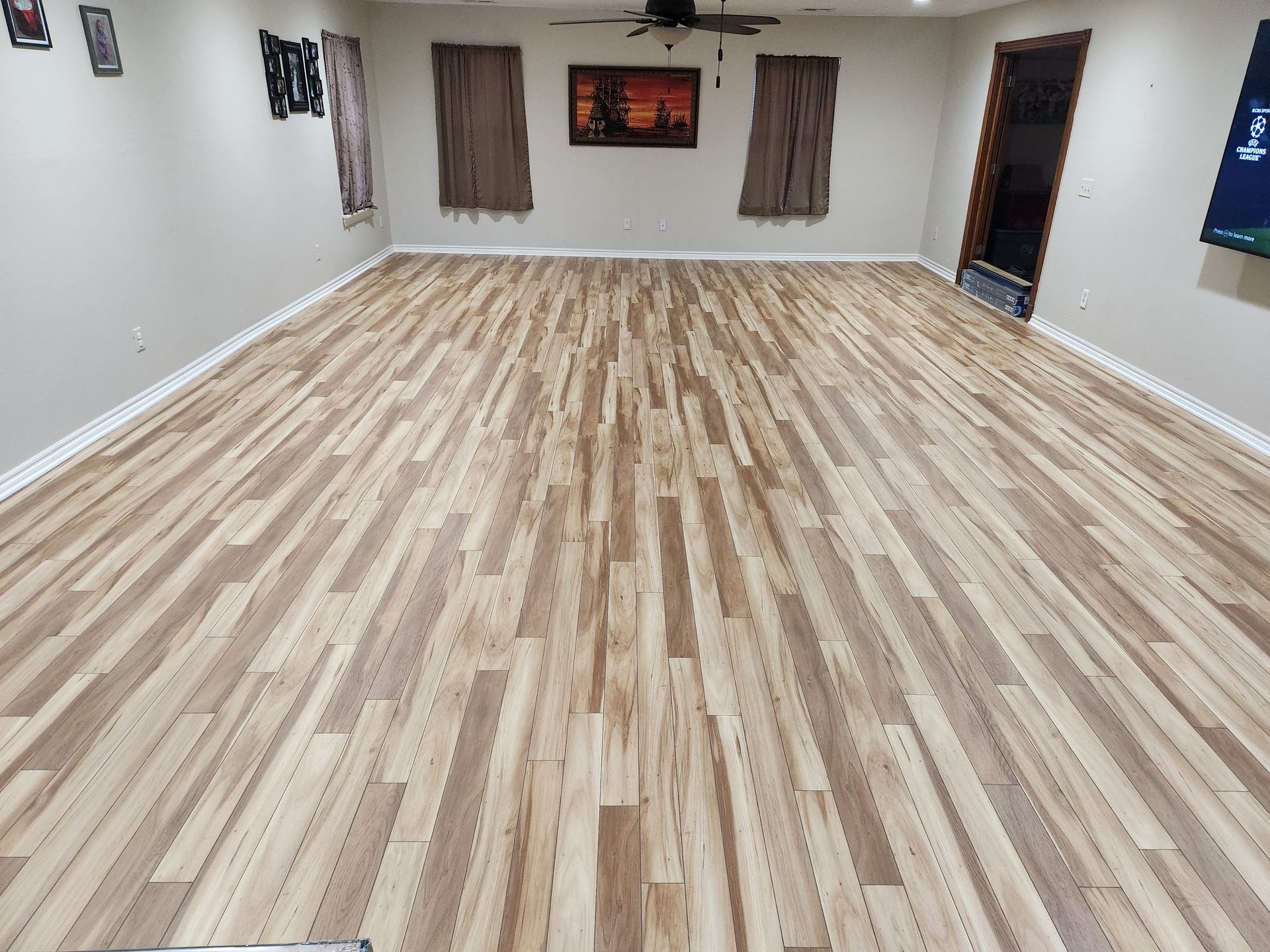 Empty room with light wood flooring, beige walls, windows, and wall art.