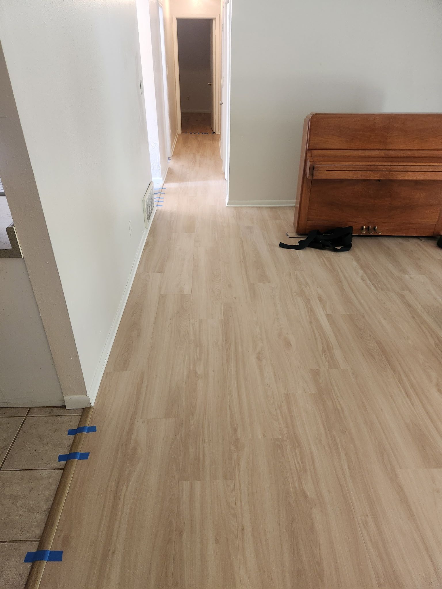 Empty hallway with light wood floor, white walls, and a brown wooden cabinet on the right.