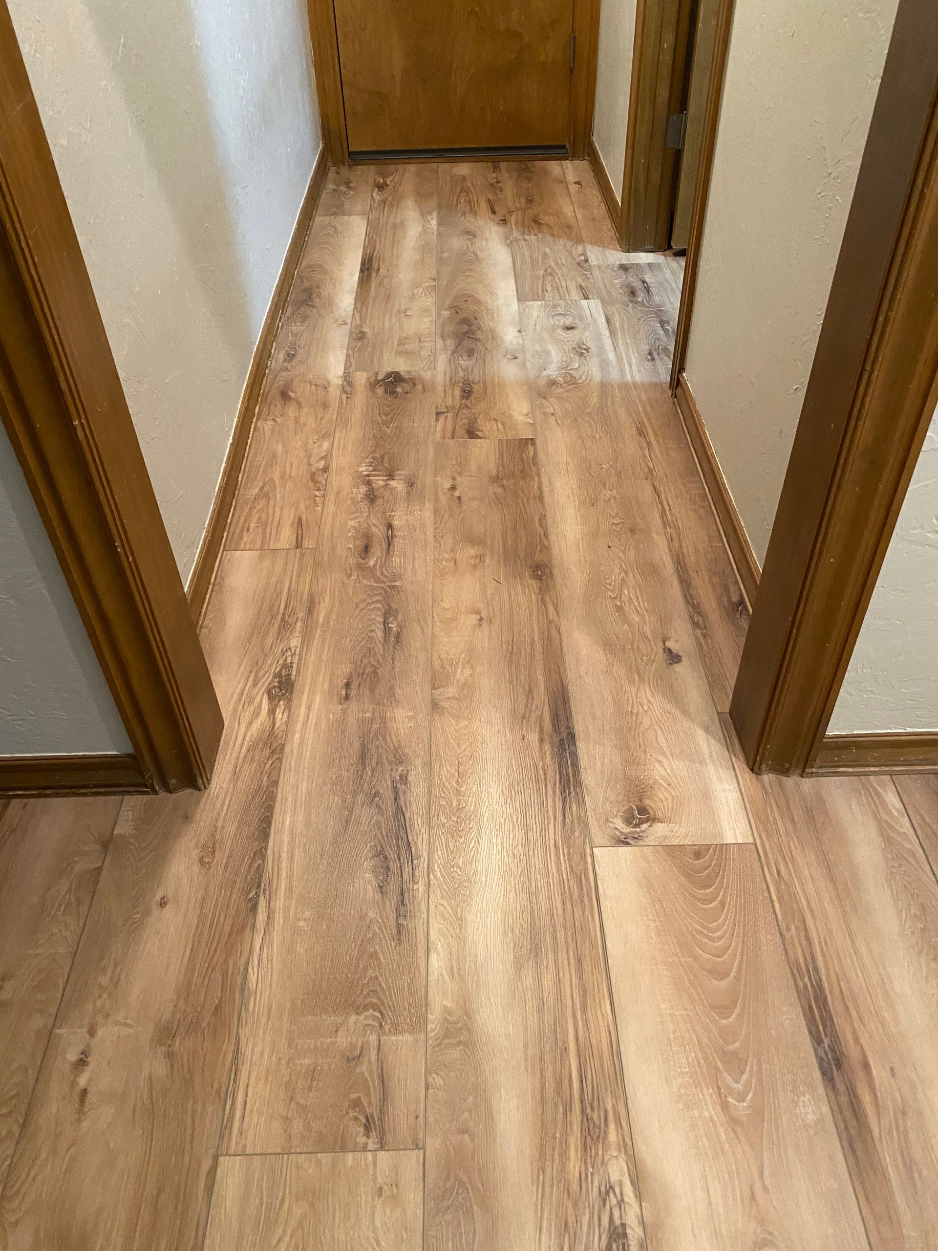 Narrow hallway with light wood flooring and doorways on both sides leading to a closed door.