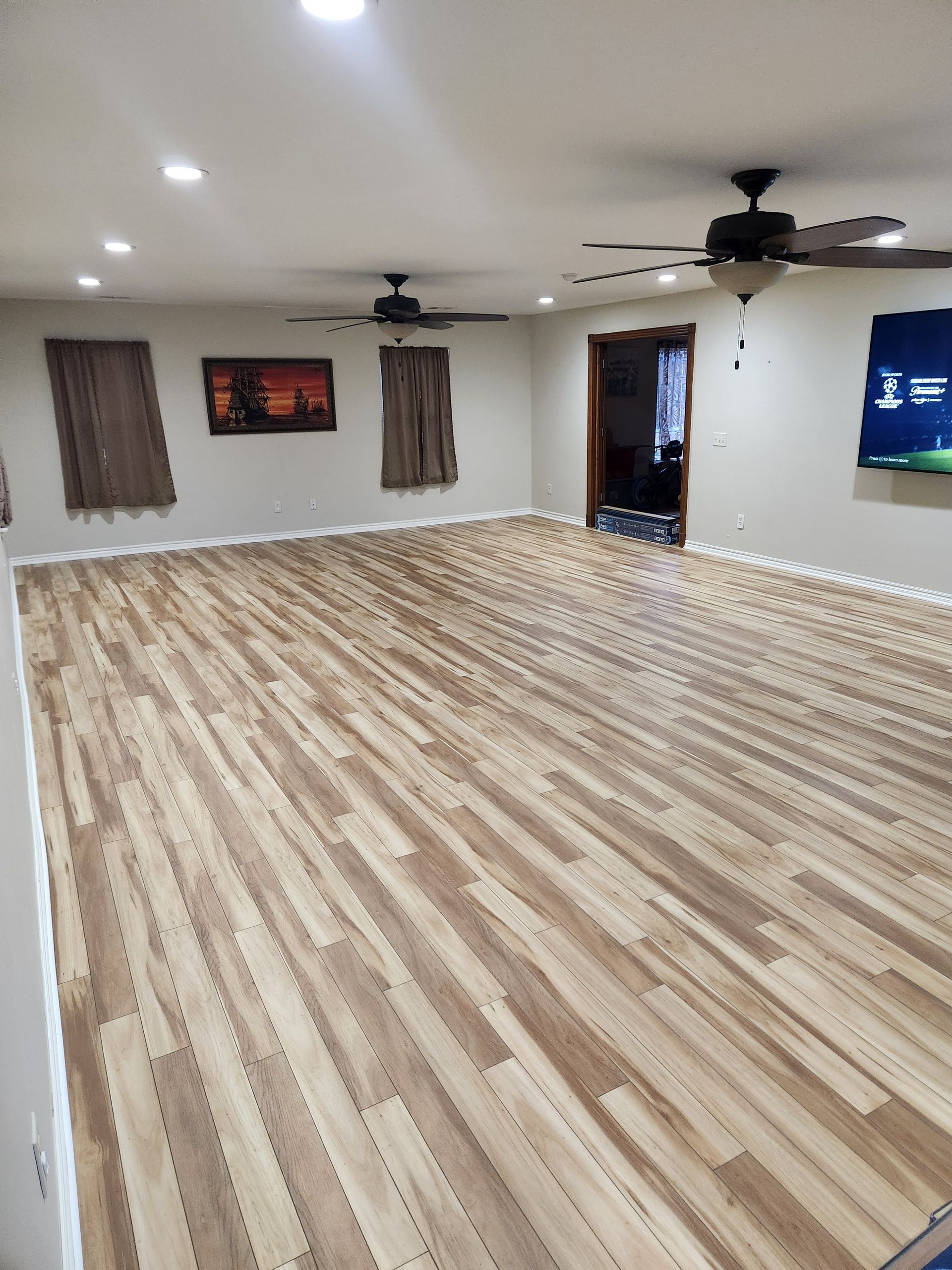 Empty living room with wood-look flooring, recessed lights, ceiling fans, and wall-mounted TV.
