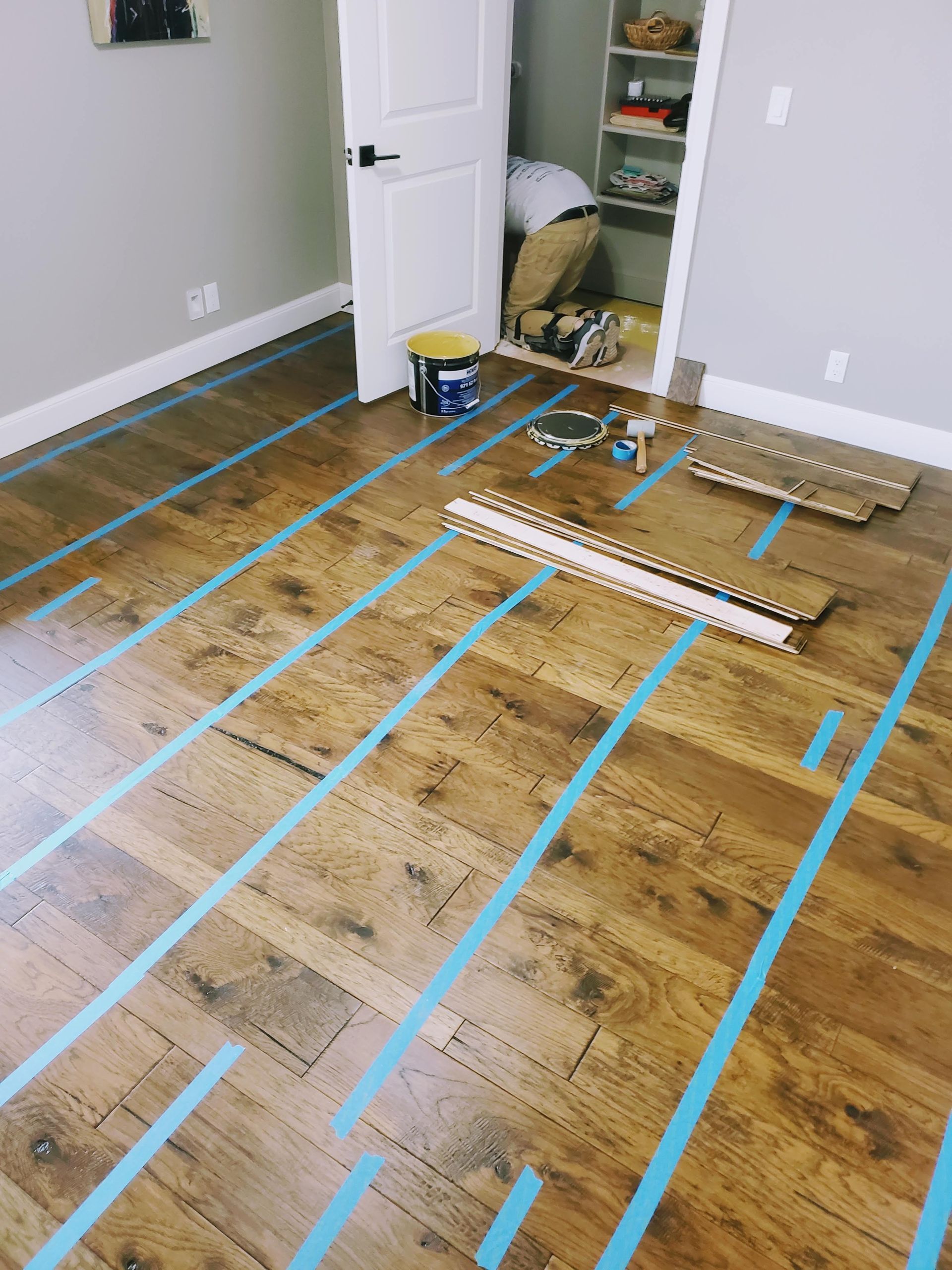 Empty room with wood floor marked by blue tape lines and a small pile of lumber near an open closet door