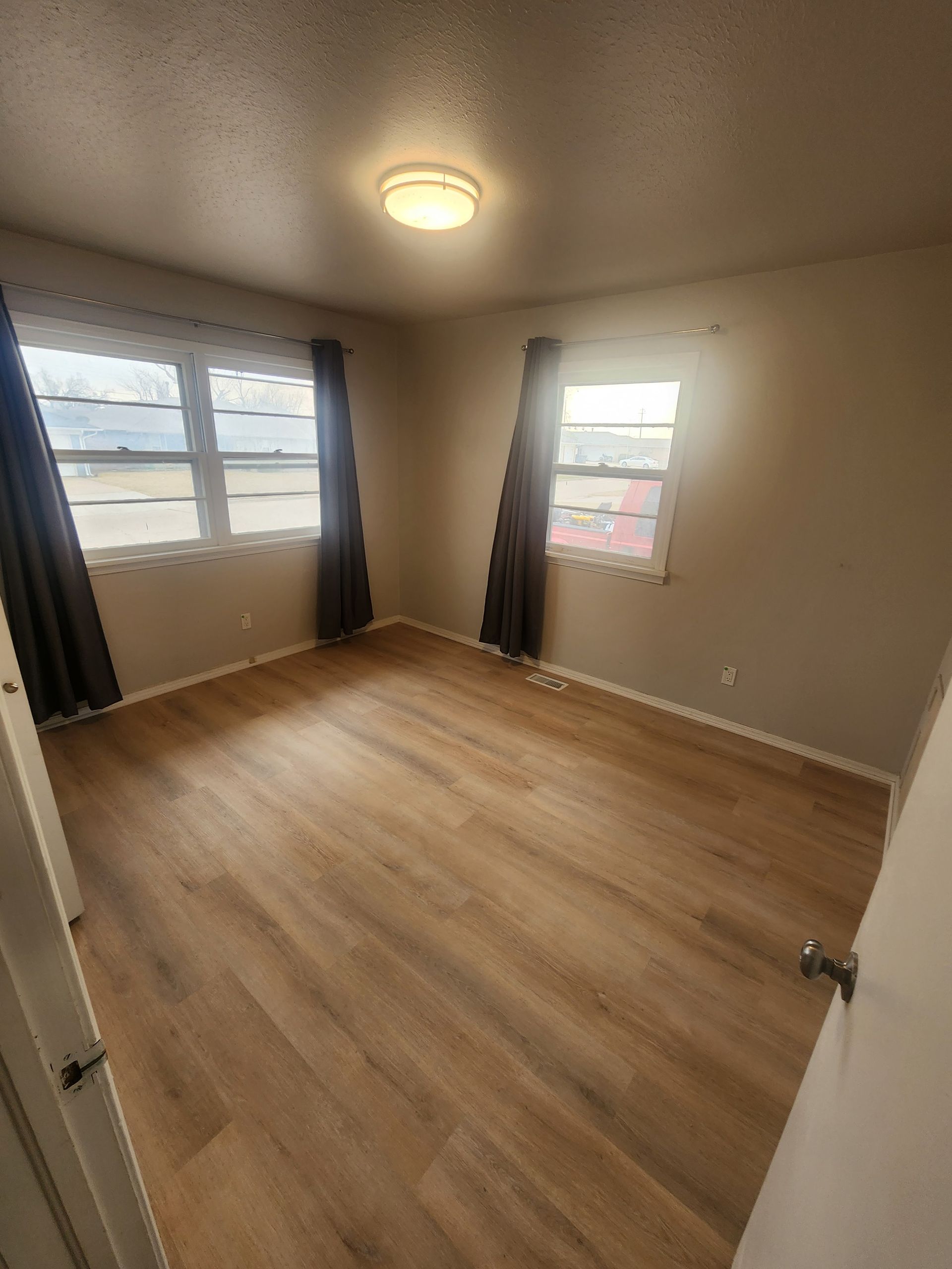 Empty beige bedroom with wood flooring, two windows, and a ceiling light