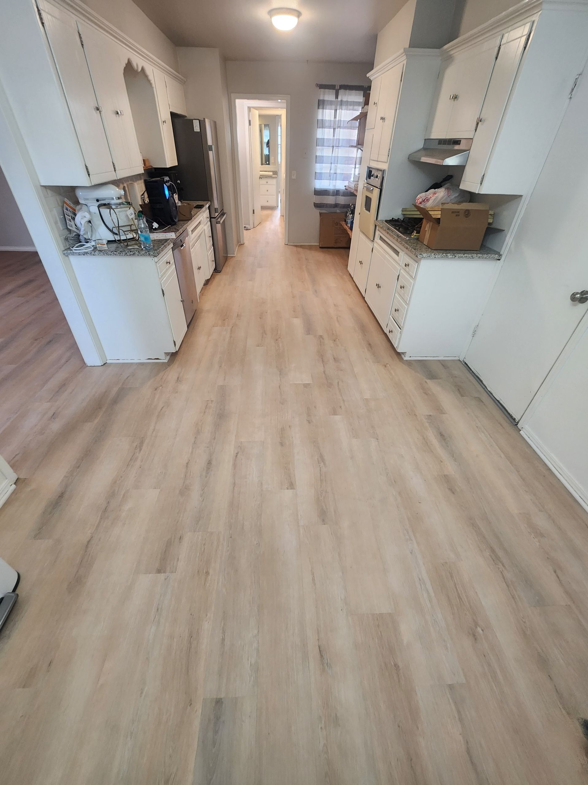 Bright hallway with light wood flooring, white cabinets, and a window at the far end.
