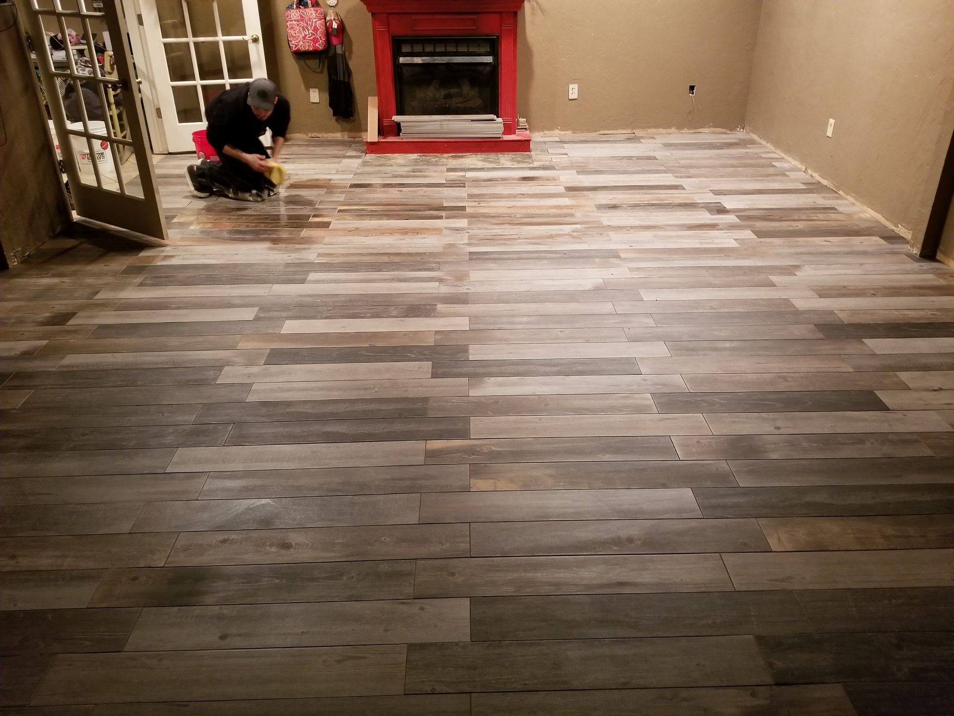 Worker installing wood floor in a room with a red fireplace