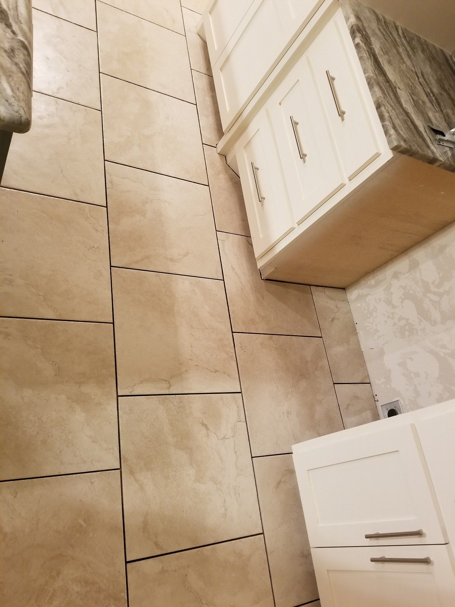 Bathroom floor with beige tiles and white cabinets on the right side.