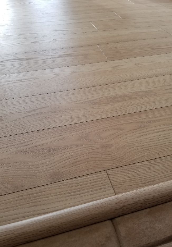 Close-up of light wood flooring with a rolled rug edge at the bottom