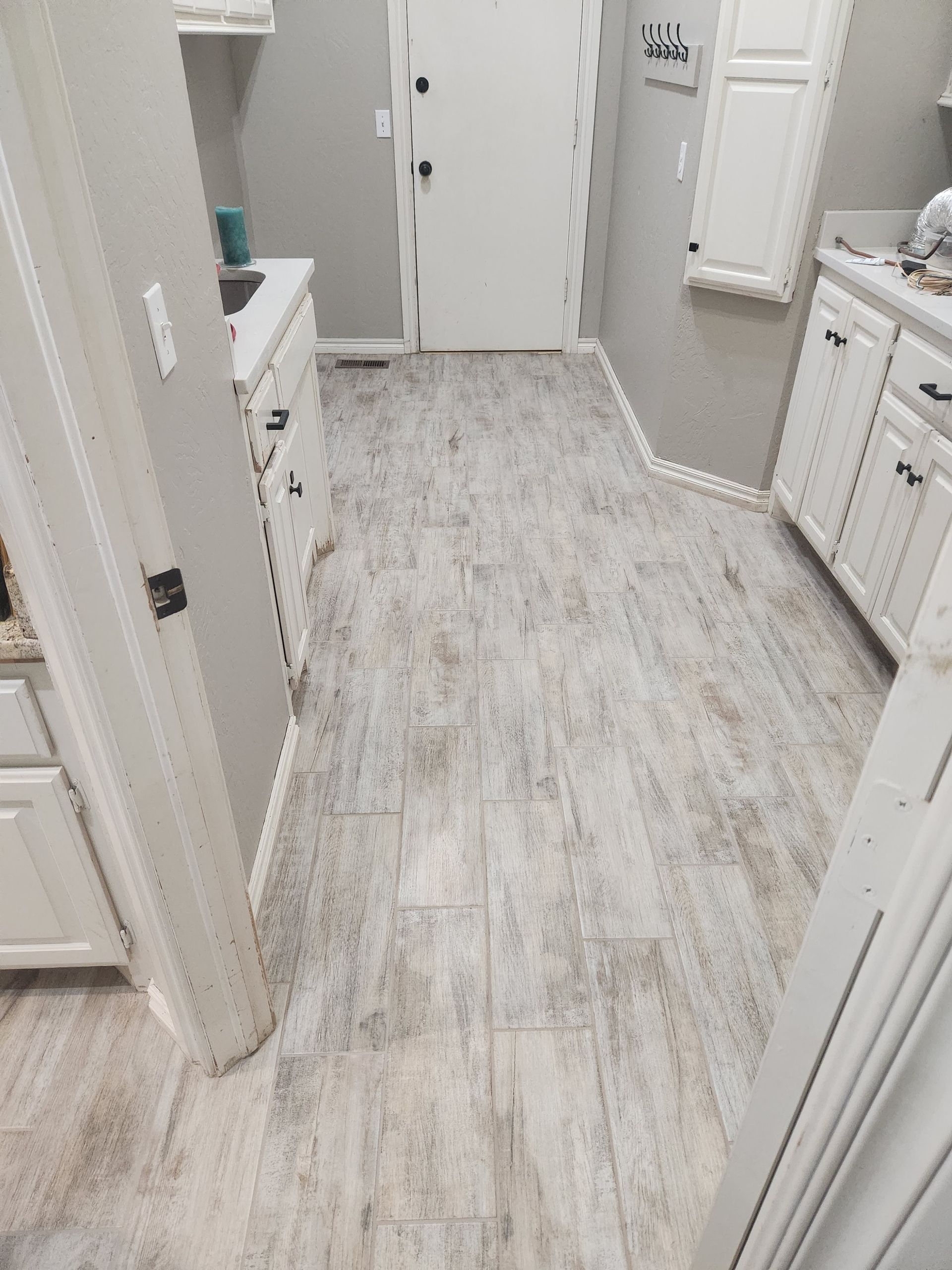 White bathroom with light wood-look tile floor, vanity cabinets, and open doorway to another room.