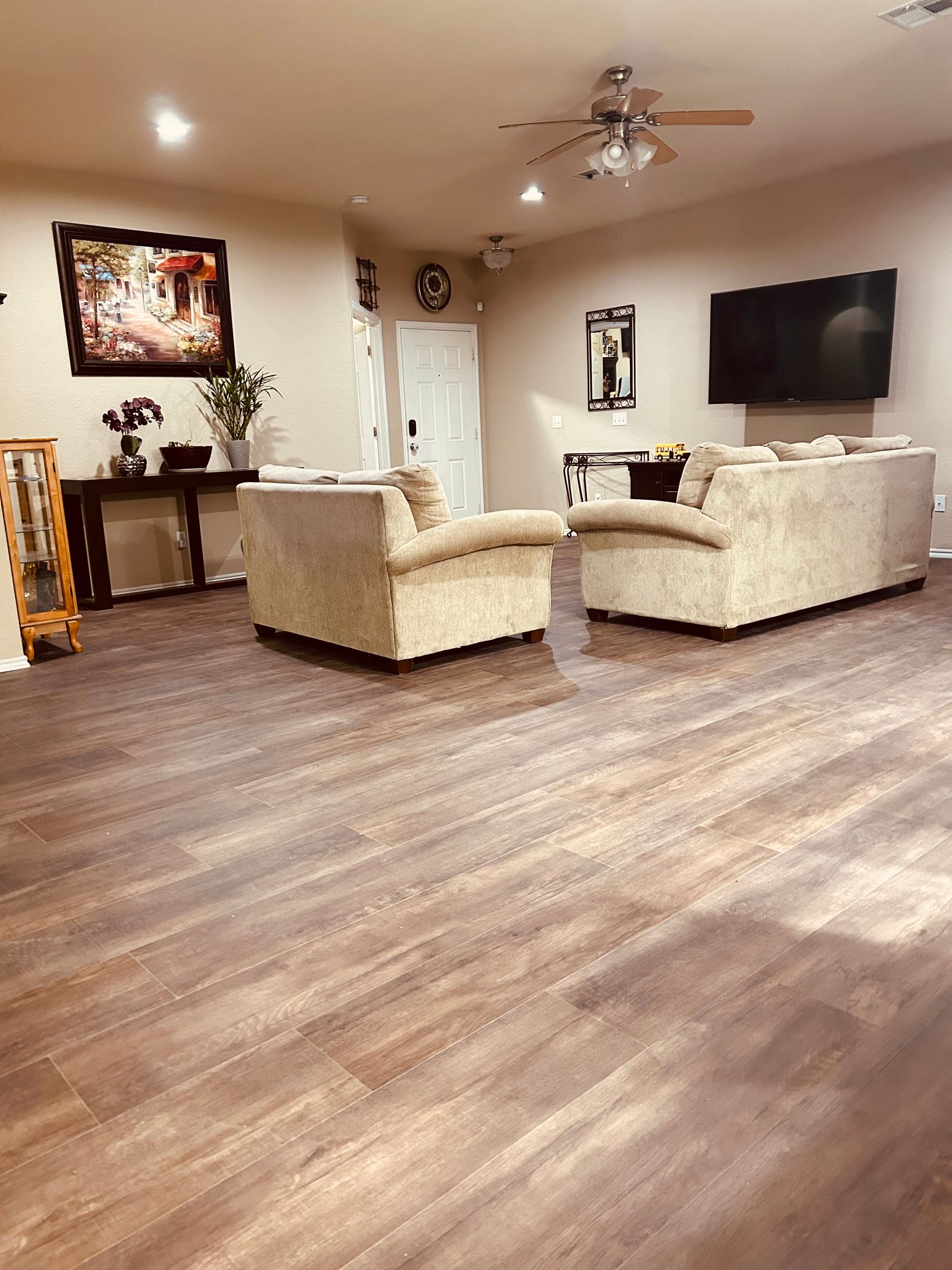 Spacious living room with beige sofas, wall-mounted TV, and wood-look flooring