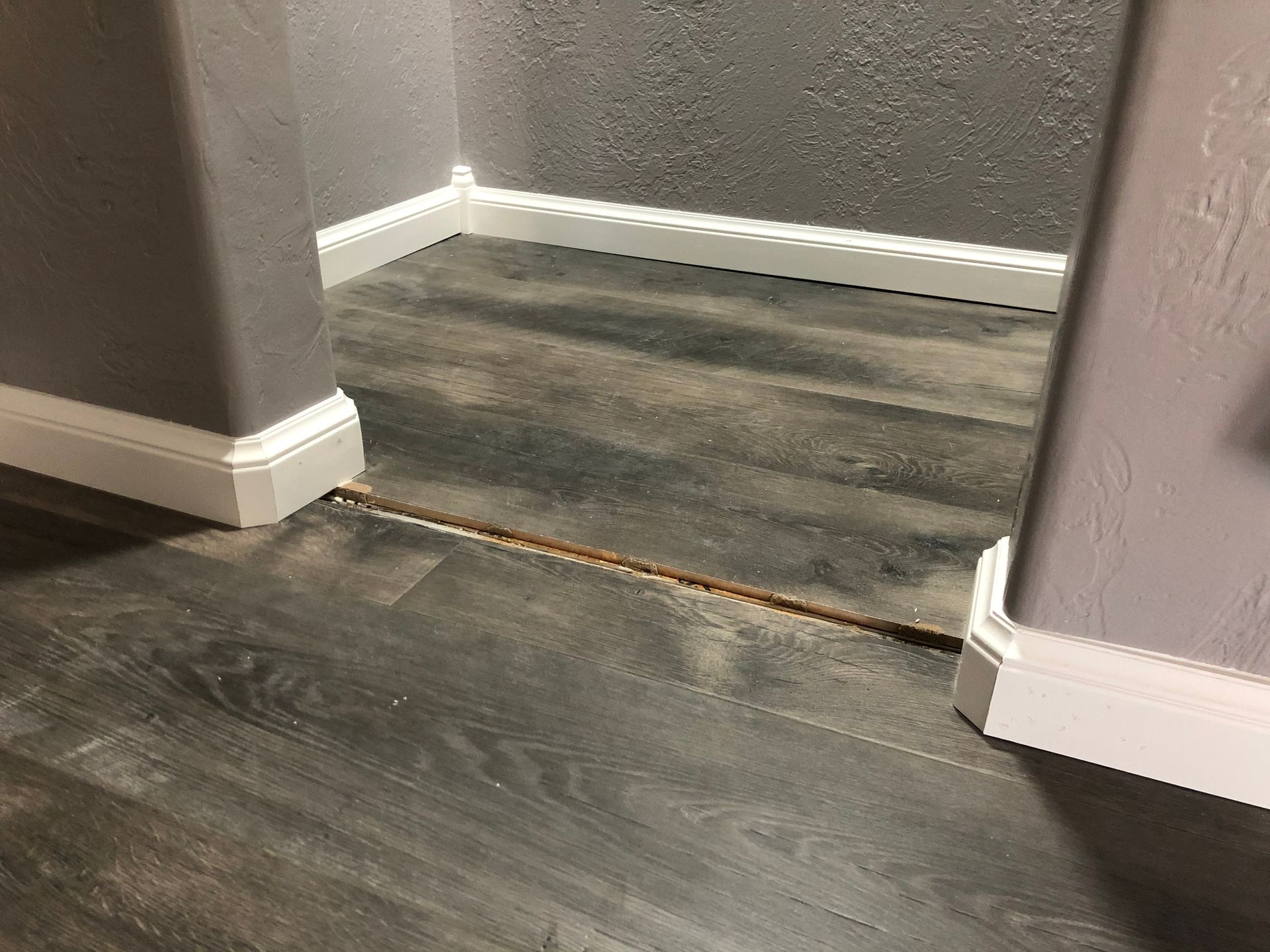 Interior doorway with a raised floor transition and dark wood flooring between gray walls