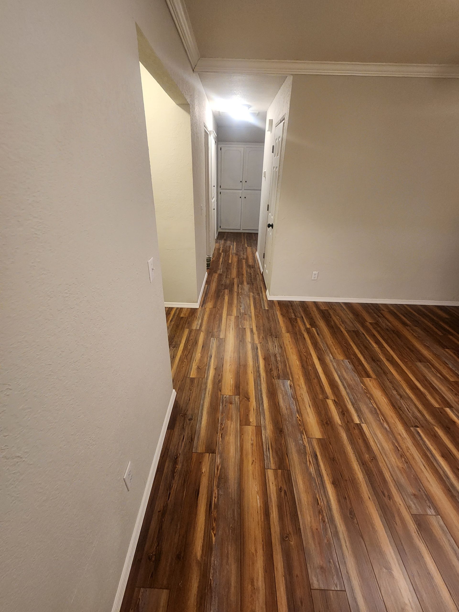 Empty hallway with glossy wood floors and white walls, lit by a bright ceiling light at the end.