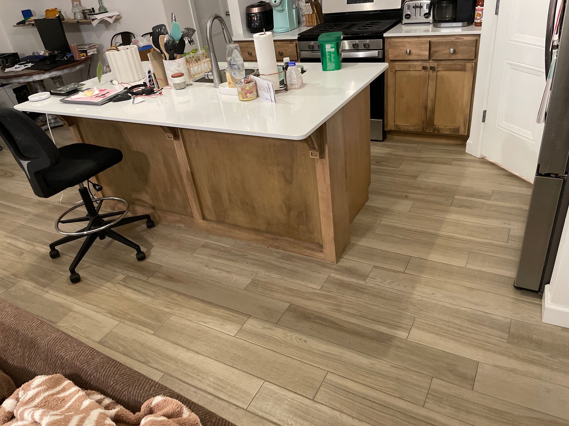Kitchen with white island, wooden cabinets, black chair, and wood-look flooring