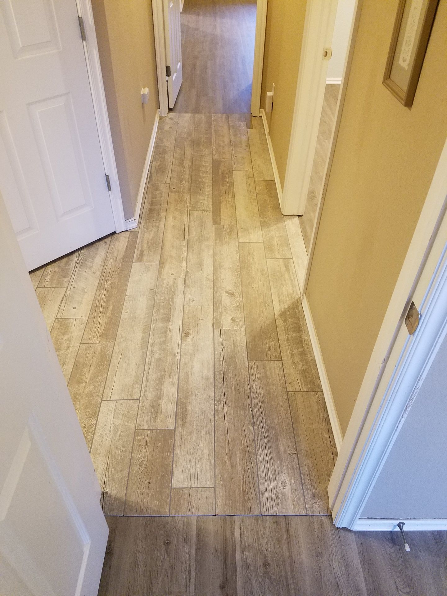 Narrow hallway with wood-look flooring, white doors, and beige walls.