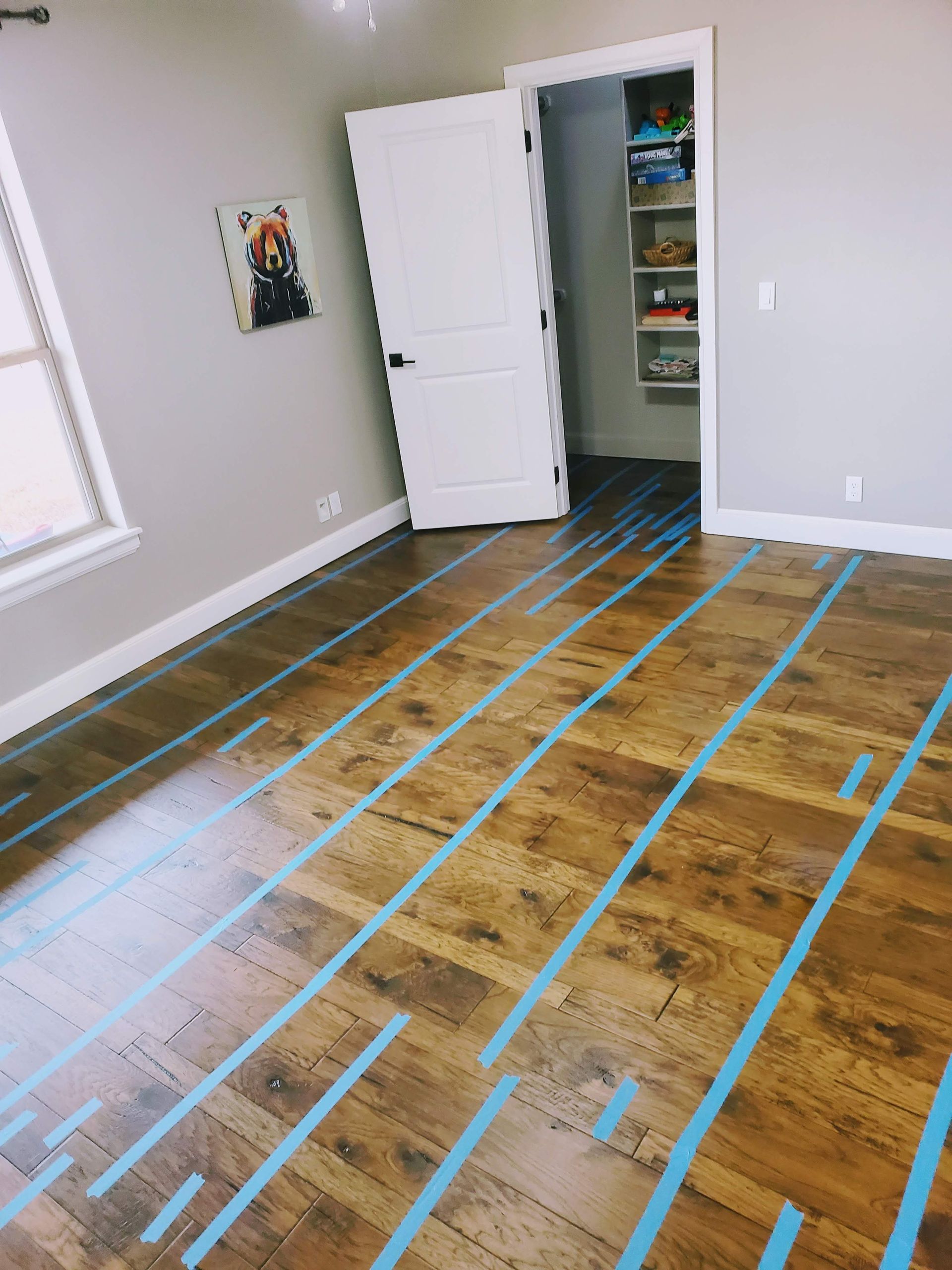 Empty room with hardwood floor marked by blue tape lines and an open white closet door.