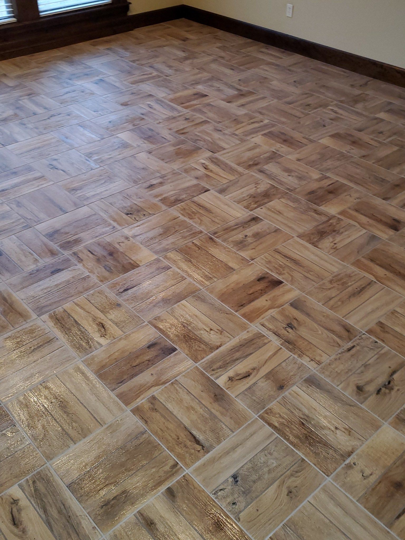 Wooden parquet floor in an empty room with brown baseboards and natural light.