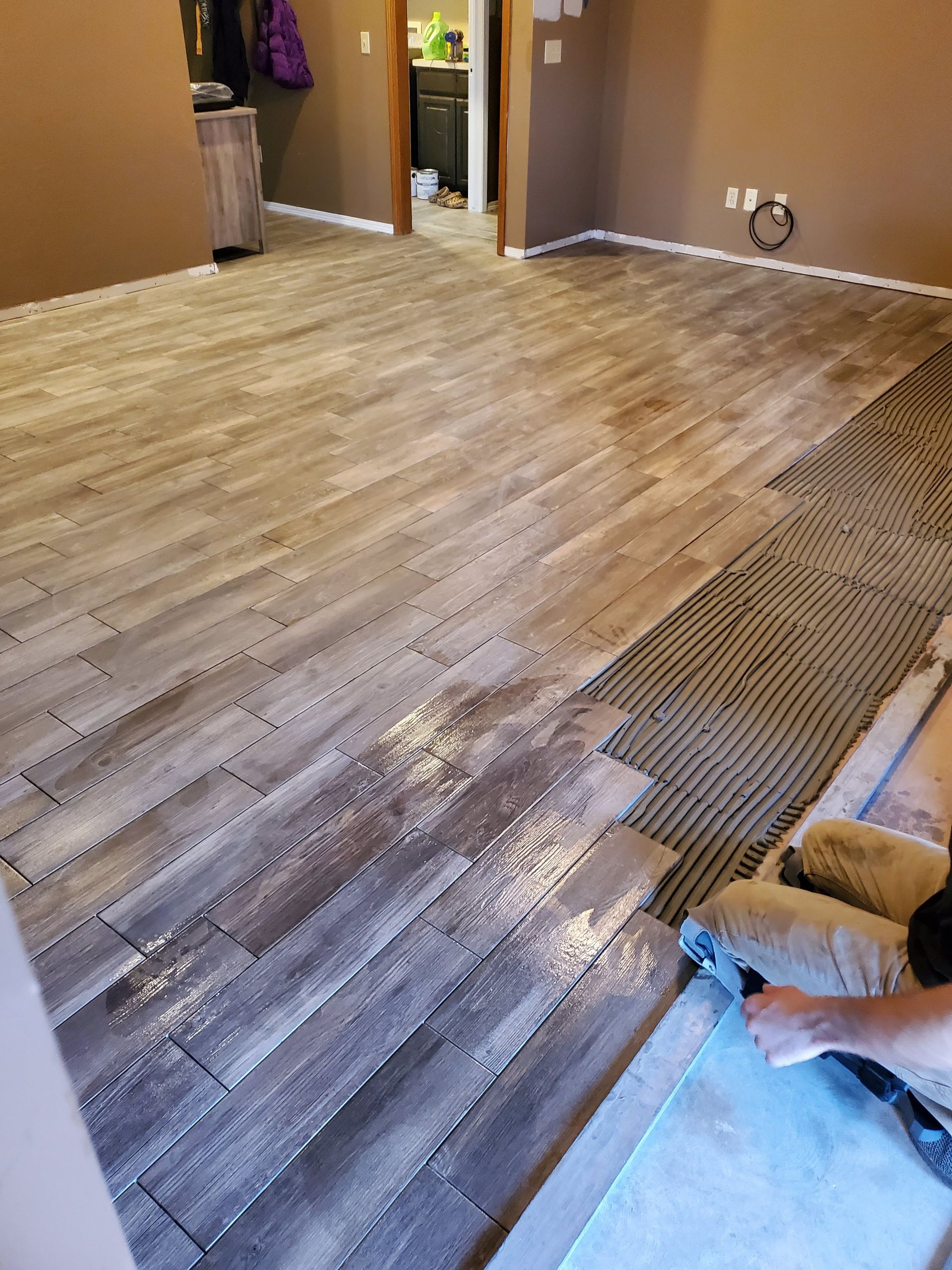 Person installing gray laminate flooring in a room with brown walls and white trim
