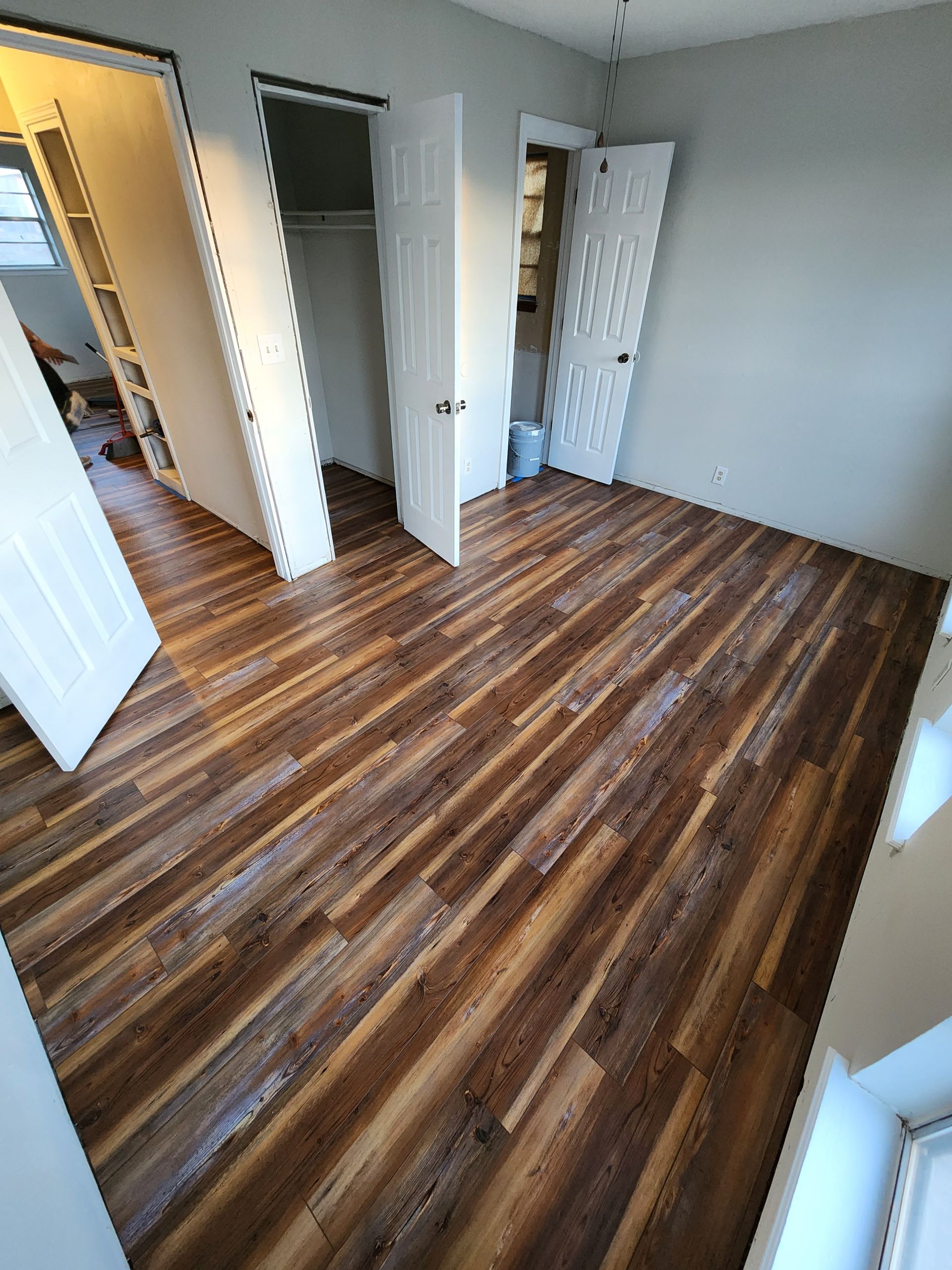 Empty room with wood-pattern flooring, gray walls, and open white doors.
