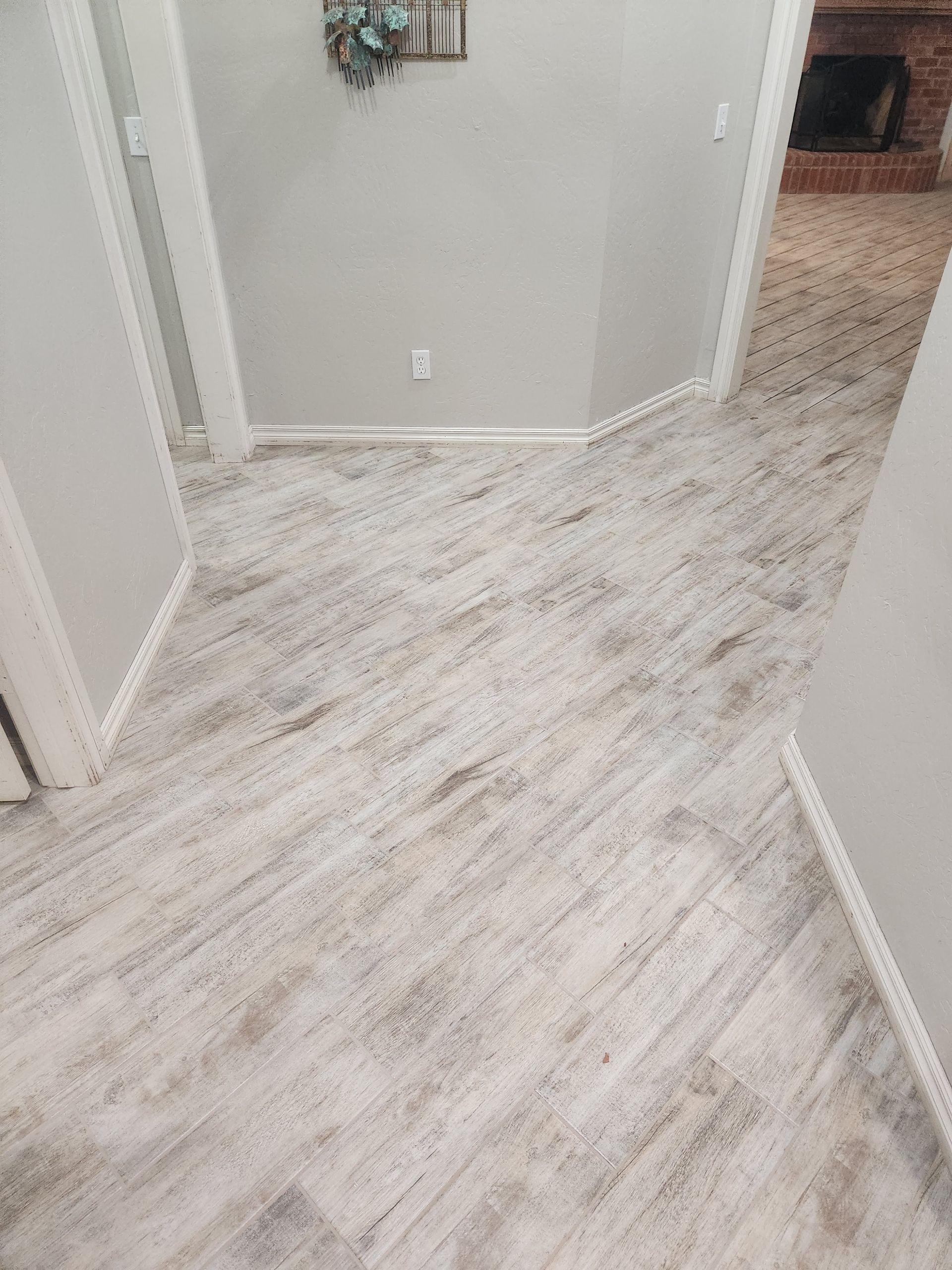 White wood-look flooring in a hallway with light gray walls and a doorway ahead.