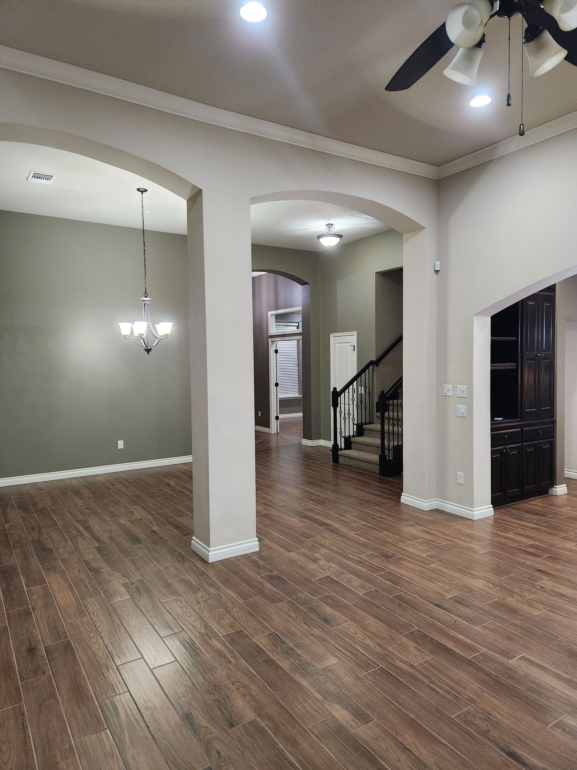 Empty living room with wood floors, arched openings, staircase, and hanging lights.