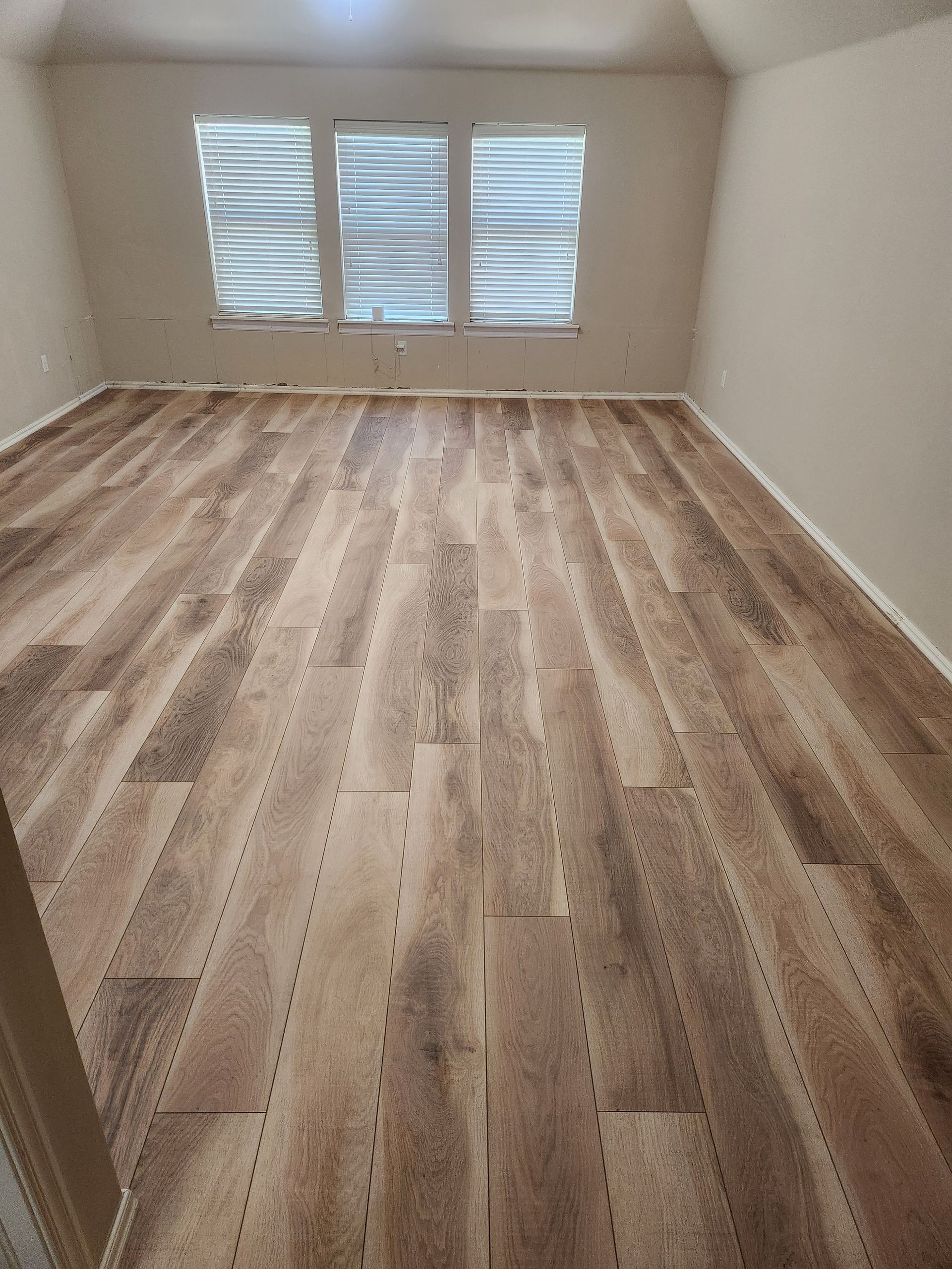 Empty room with wood-look floor and three windows with white blinds