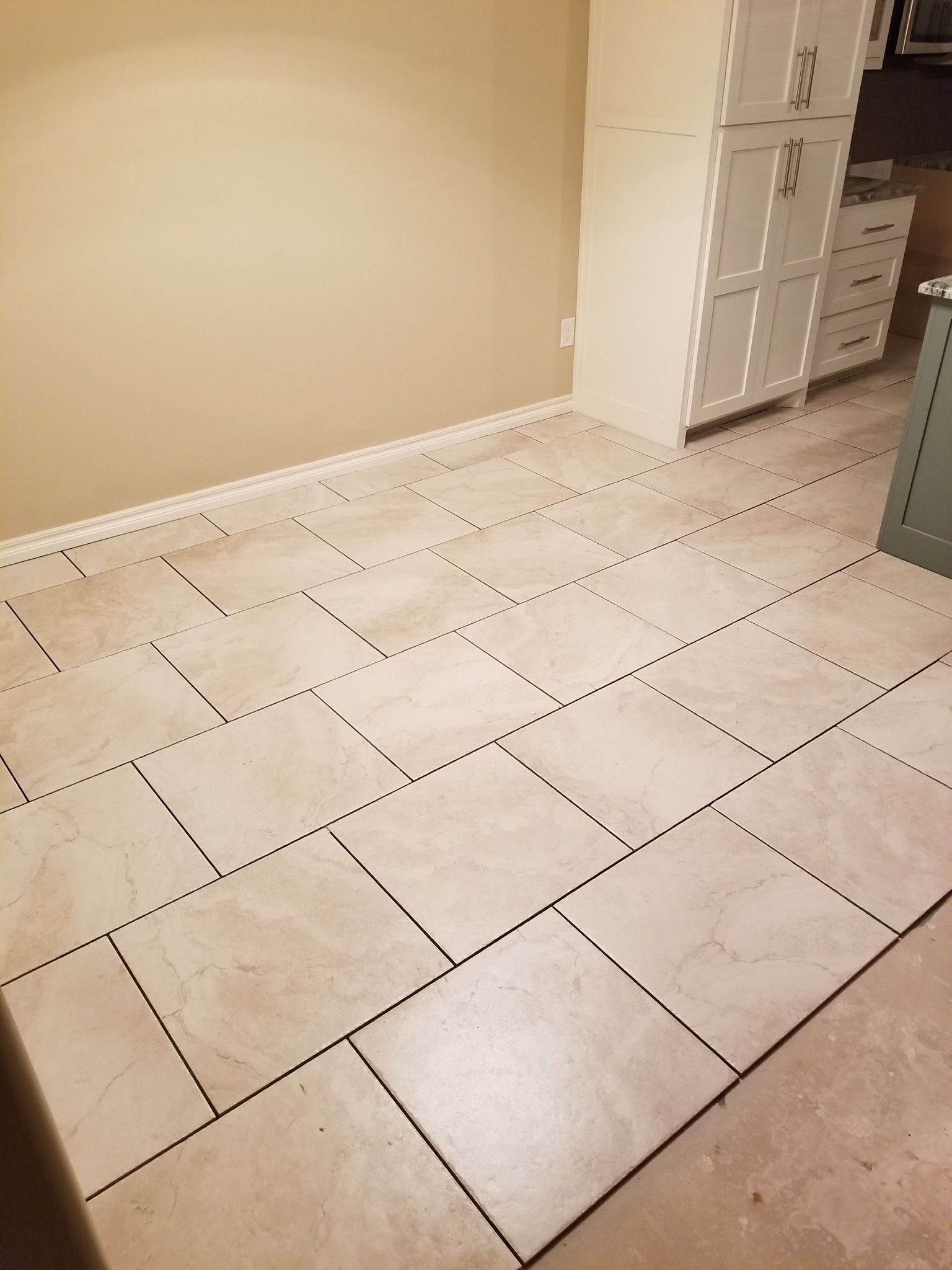 Empty tiled room with beige walls and white cabinets along the right side.